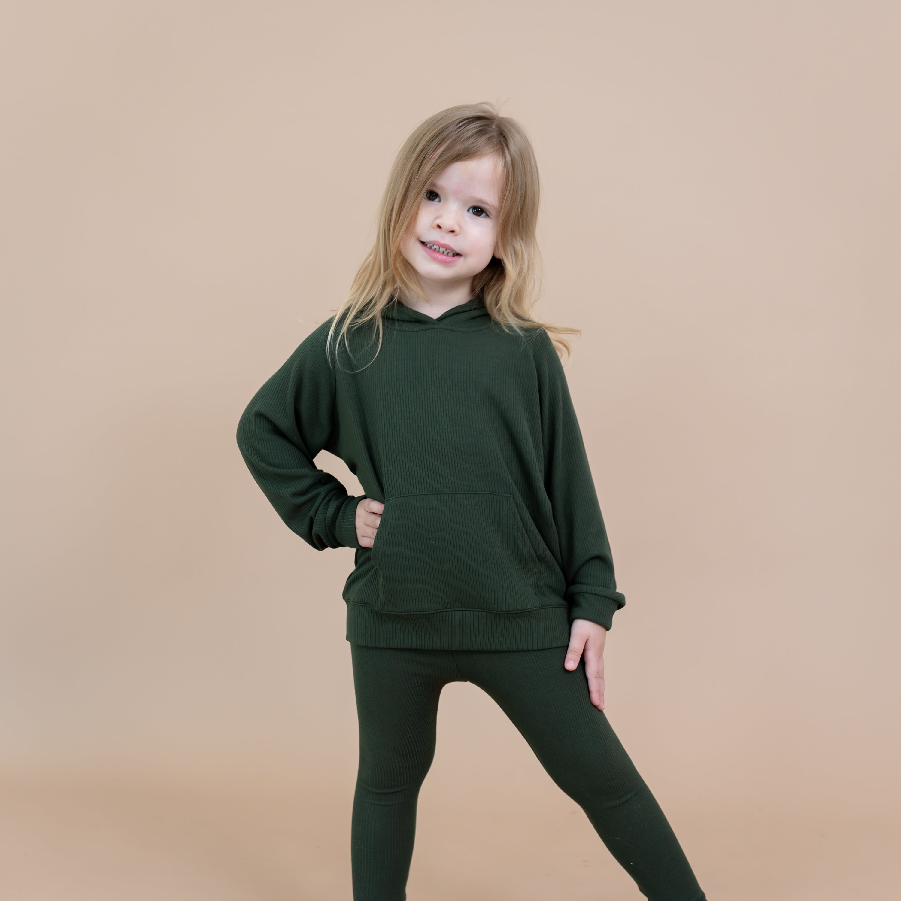 Young girl posing with one arm on her hip with the other on the top of her leg wearing the Ribbed Hoodie in Fir and matching ribbed leggings