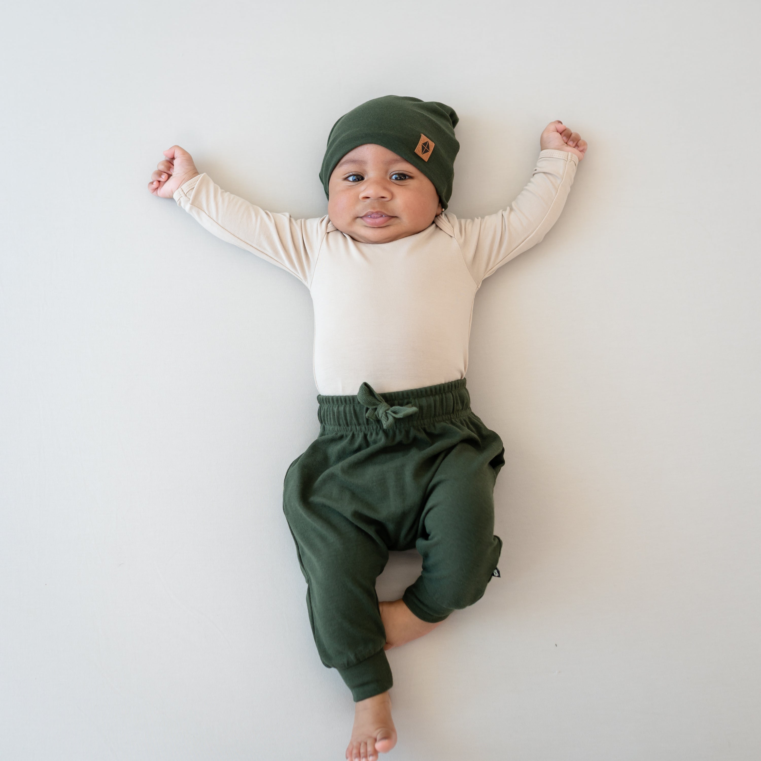 Infant wearing Bamboo Jersey Harem Pants in Fir and matching beanie with long sleeve onesie
