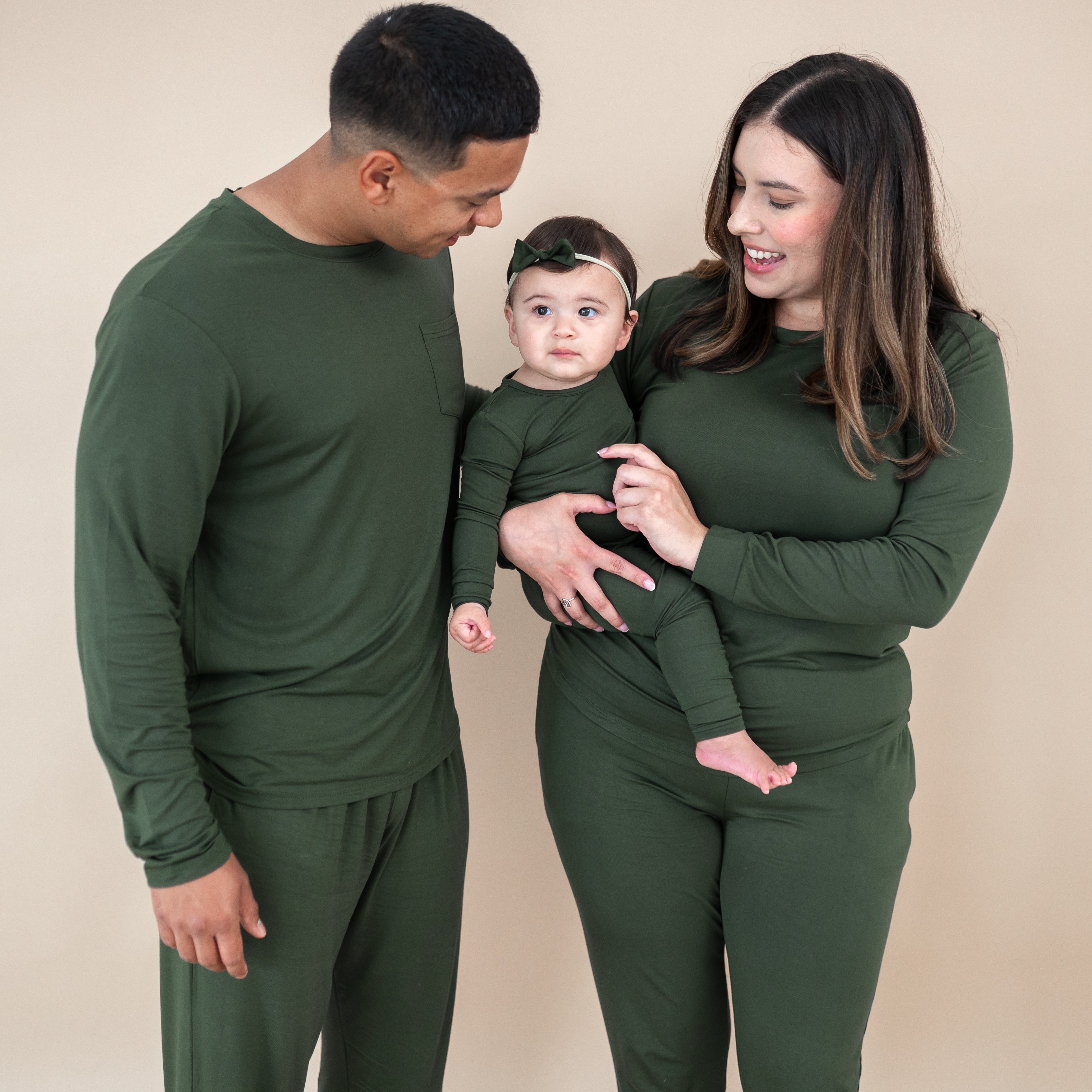 Family of three wearing matching green outfits against a beige background