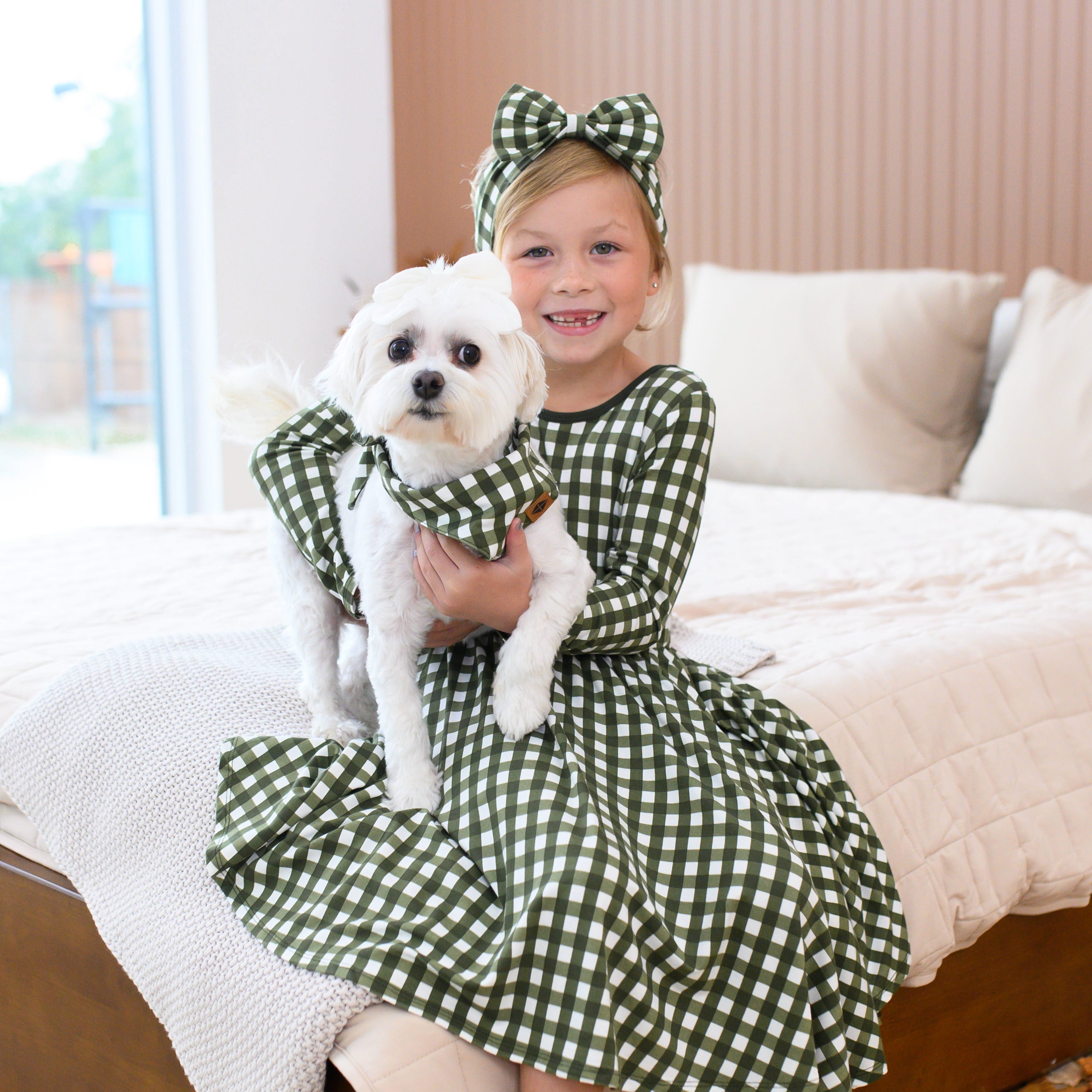 Girl wearing Gingham Christmas dress and bow headband holding dog in matching bandana