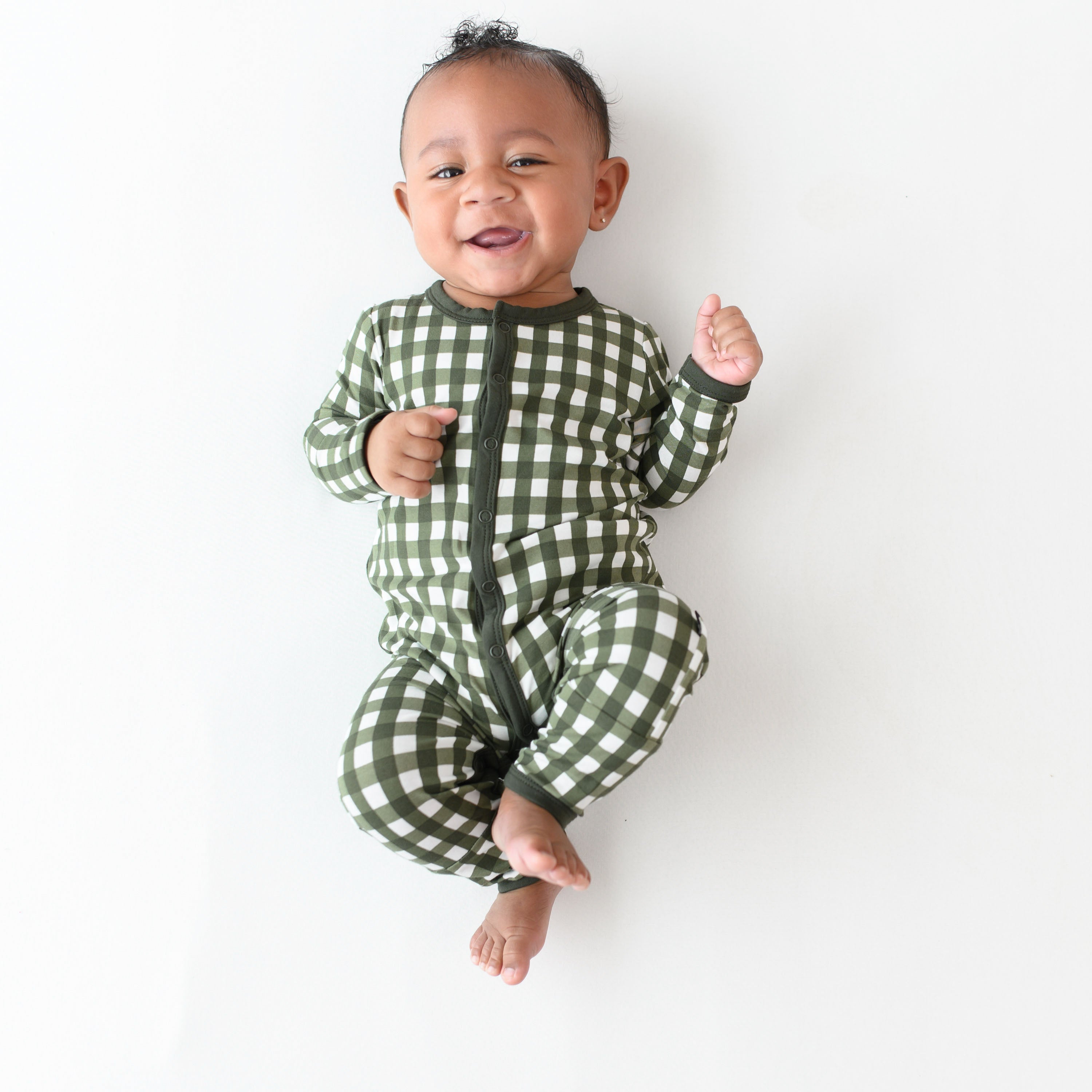 Smiling infant laying down wearing the Romper in Gingham Fir