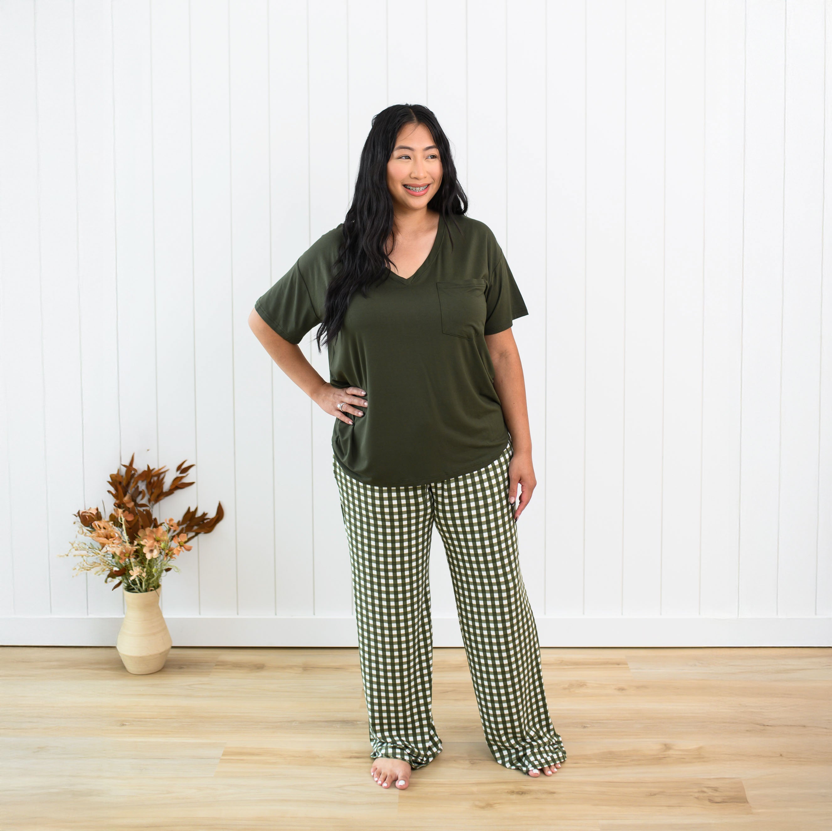 Female model standing with one hand on her hip in front of a white paneled wall wearing the Women's Lounge Pants in Gingham Fir