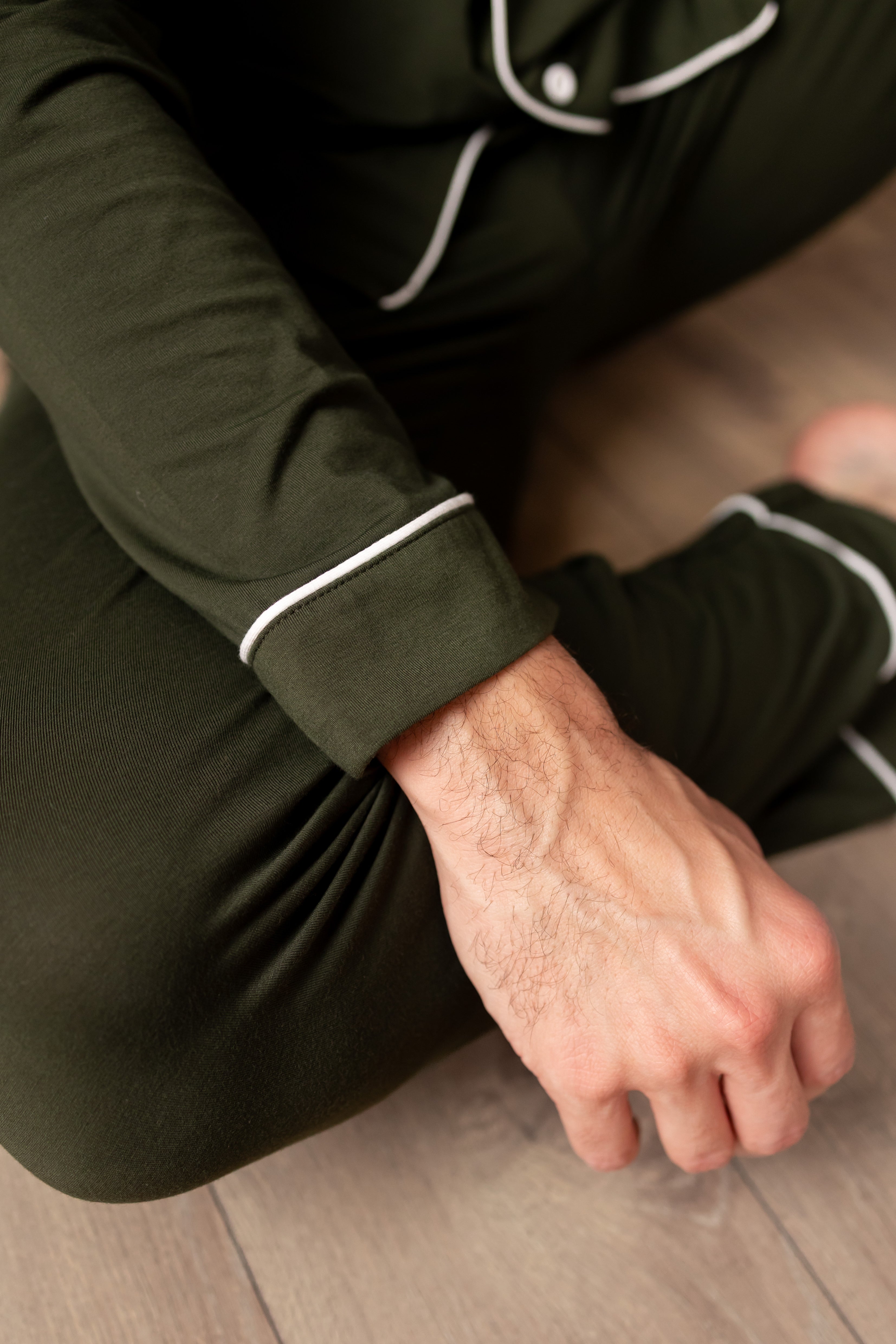 Person wearing dark green pajama set with white trim sitting on a wooden floor.