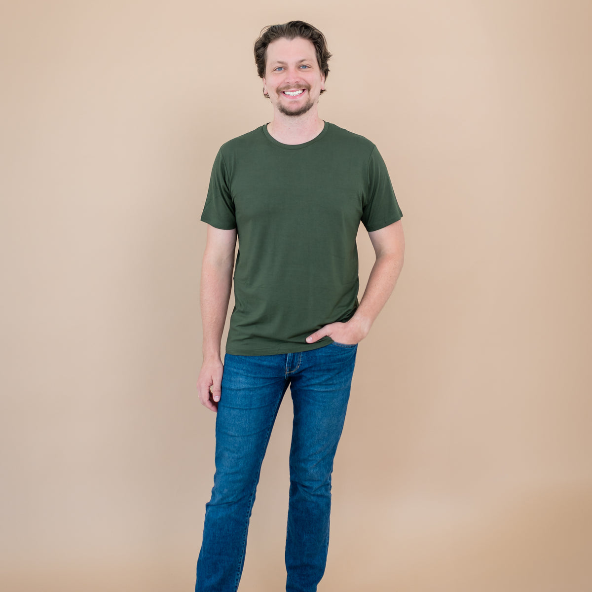 Man wearing a green t-shirt and blue jeans against a beige background