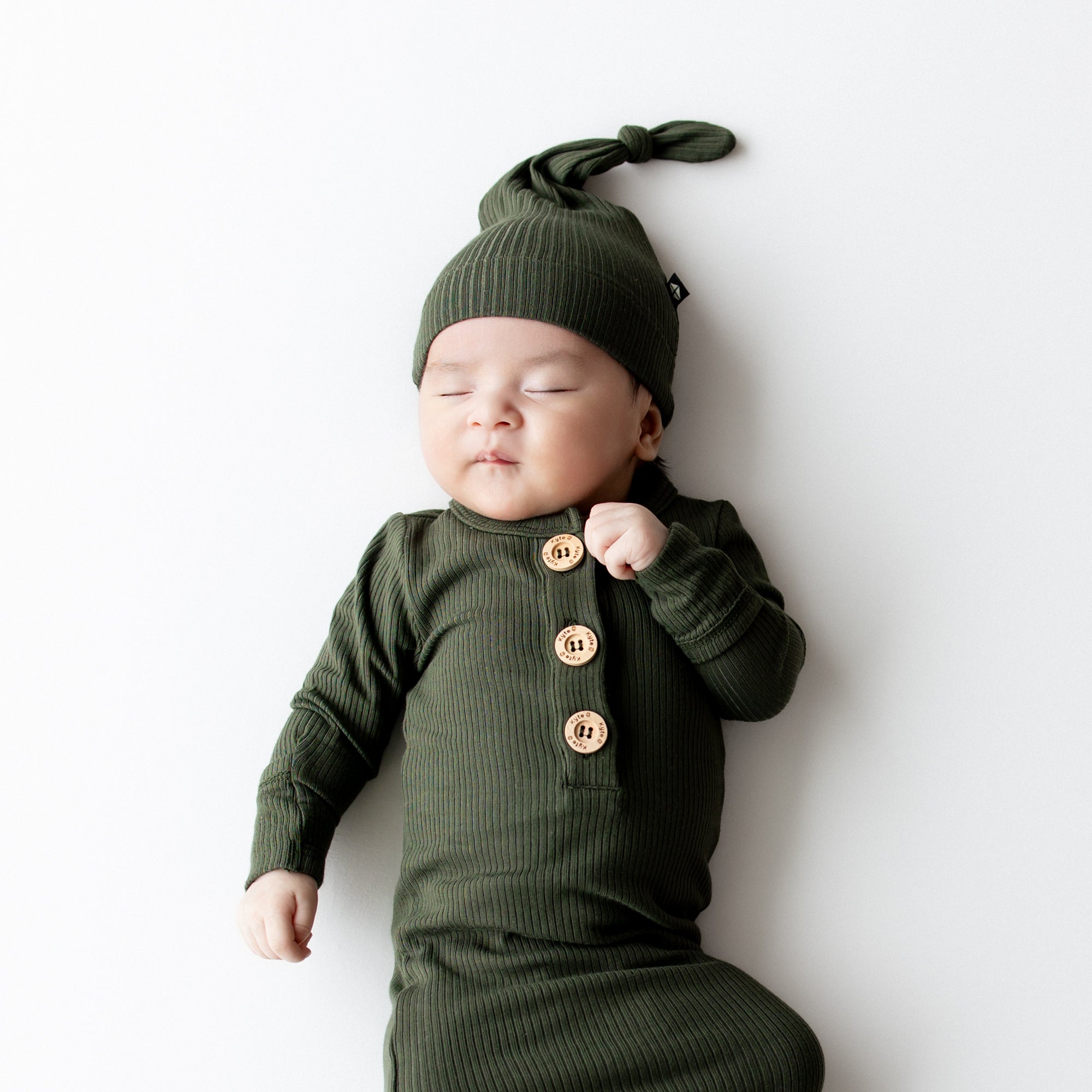 Close up of sleeping infant wearing the Ribbed Knotted Gown with Hat Set in Fir on a light colored back drop