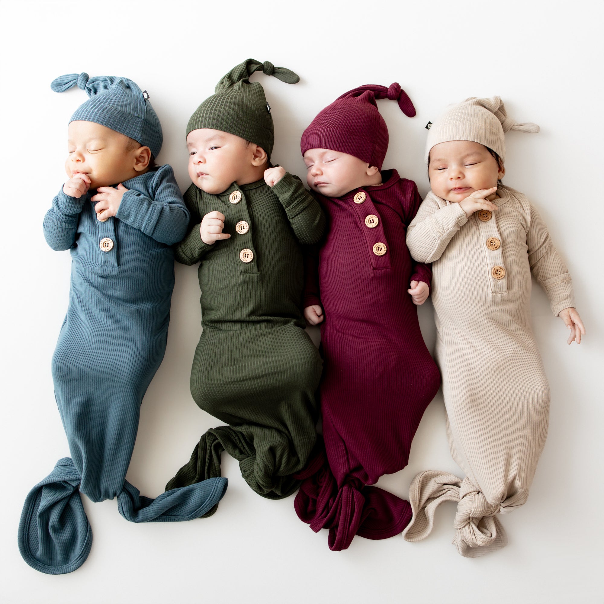 Four infants laying side by side wearing the Ribbed Knotted Gown with Hat Sets in Atlantic, Fir, Burgundy and Bisque