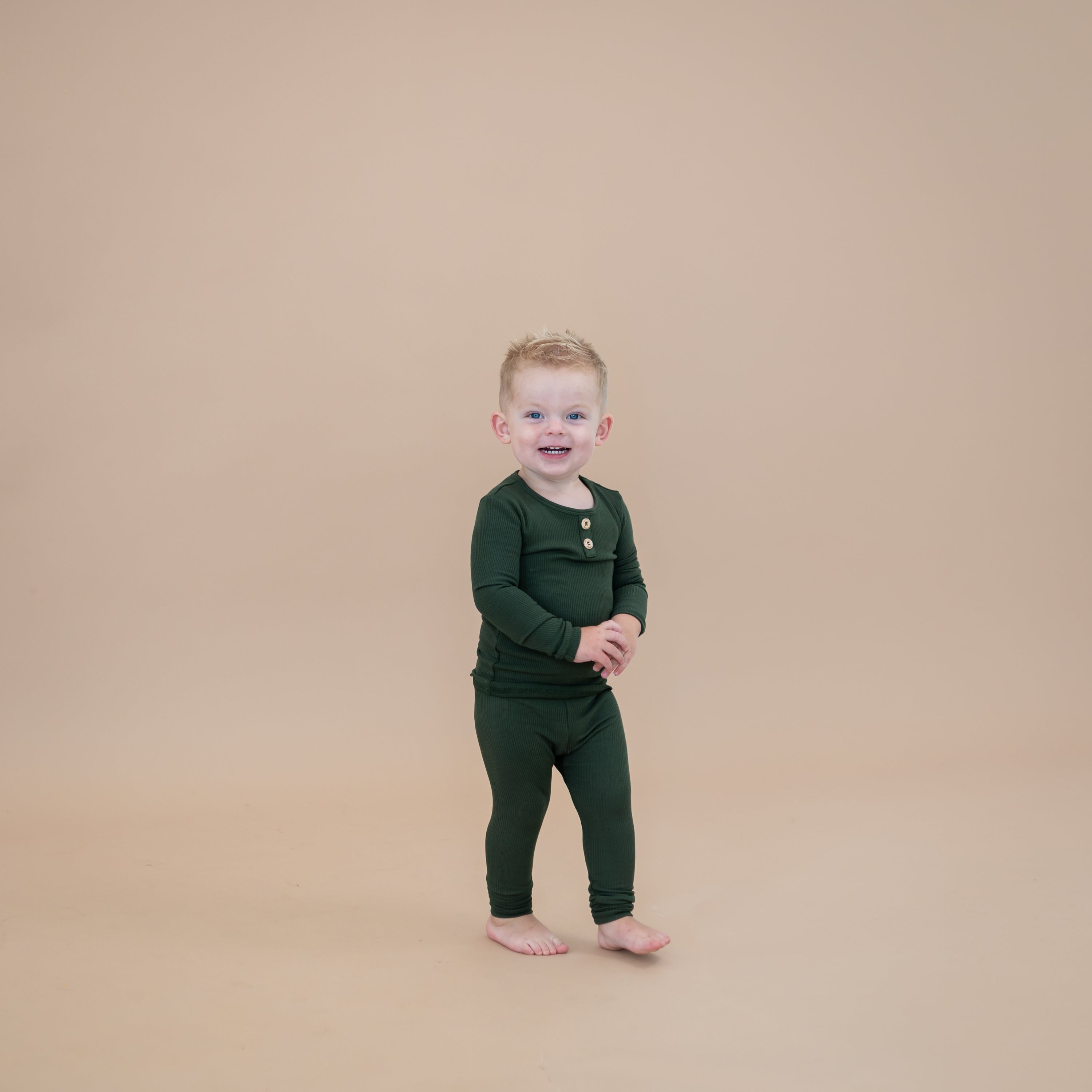 Toddler walking wearing the Ribbed Henley Set in Fir in front of a taupe colored backdrop