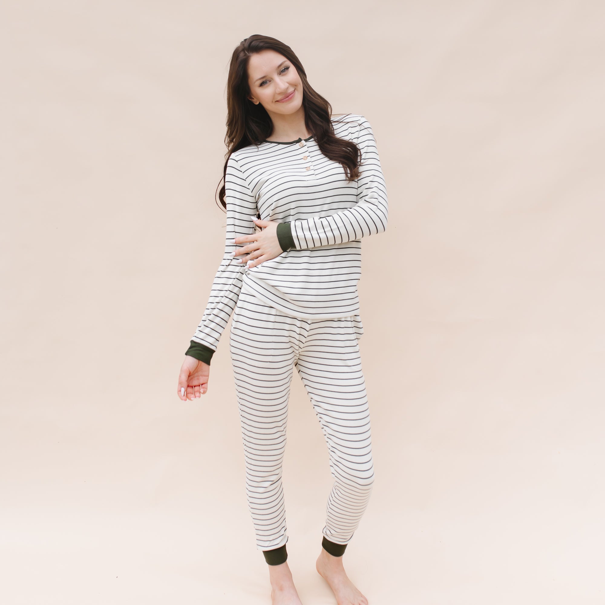 Smiling female model standing in front of a light beige background wearing the Women’s Ribbed Henley Set in Fir Stripe