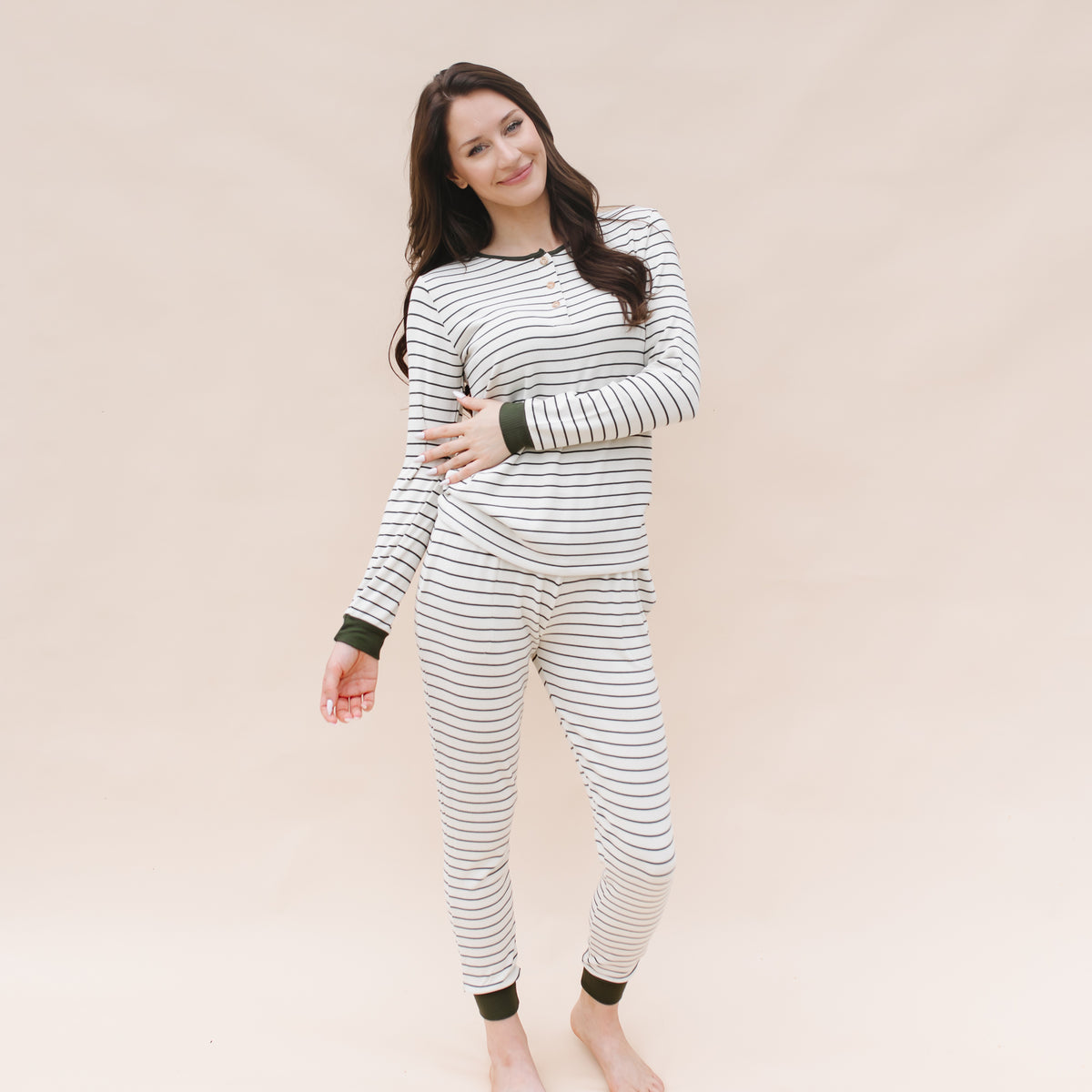Smiling female model standing in front of a light beige background wearing the Women’s Ribbed Henley Set in Fir Stripe