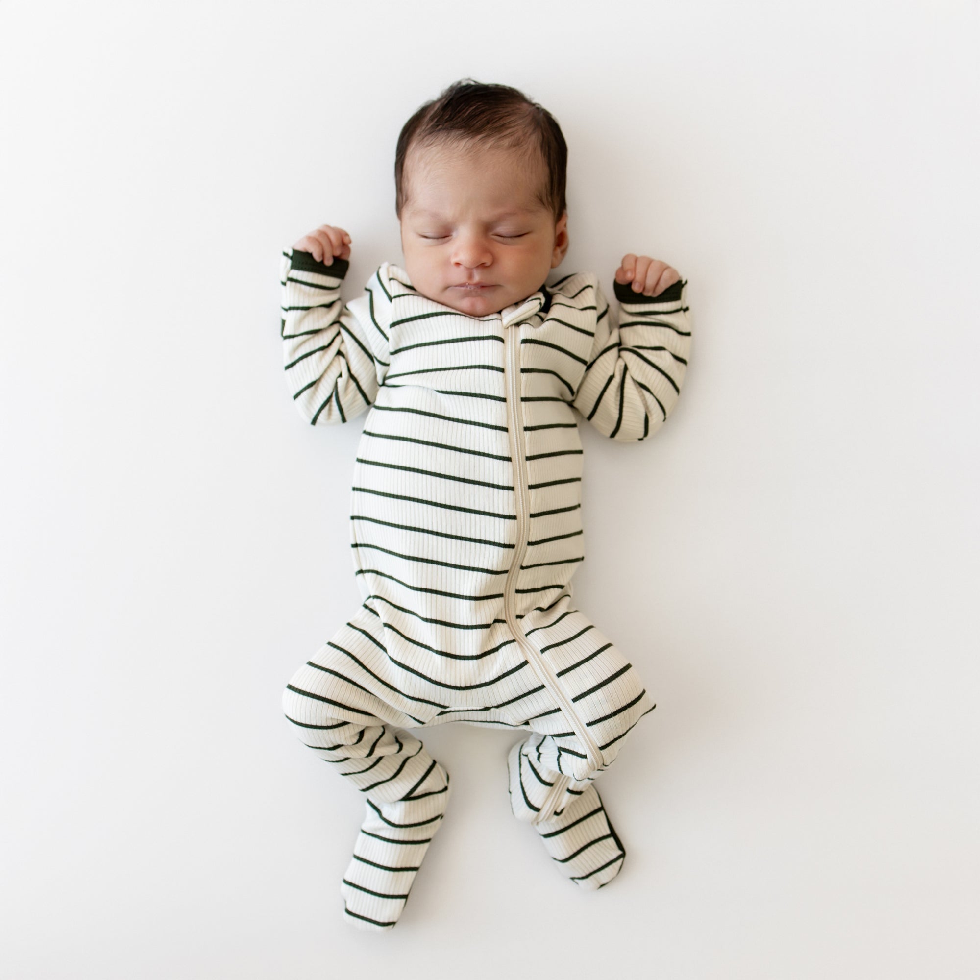 Sleeping newborn laying on a cream blanket wearing the Ribbed Zipper Footie in Fir Stripe