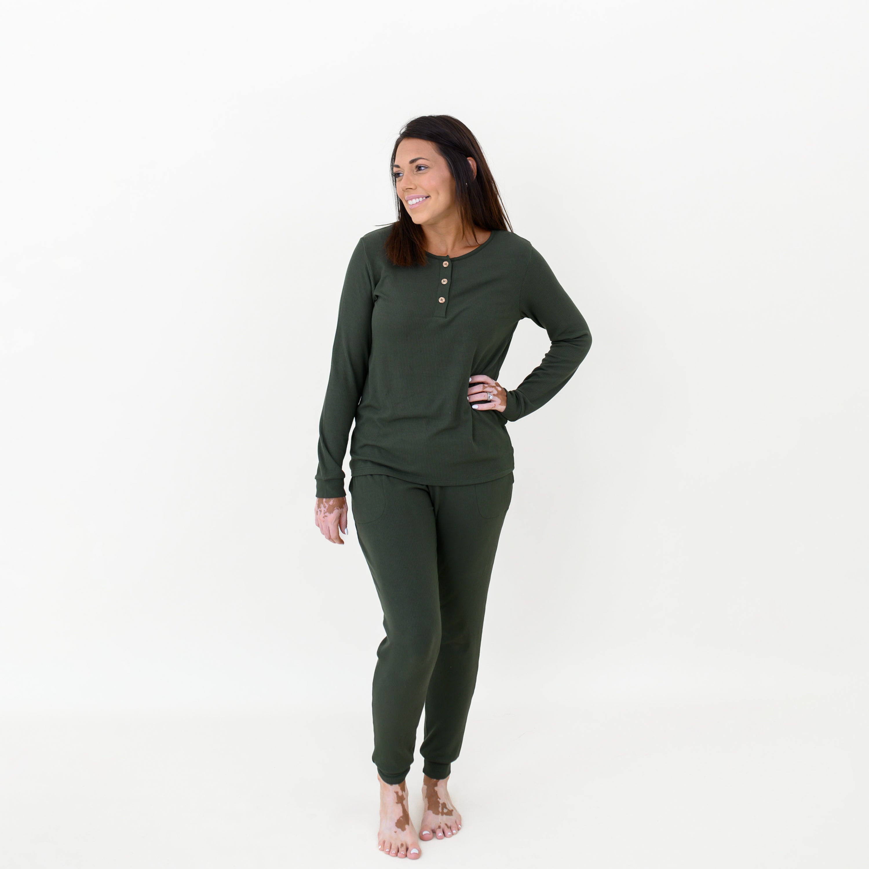 Female model standing with one hand on her hip wearing the Women’s Ribbed Henley Set in Fir in front of a white backdrop