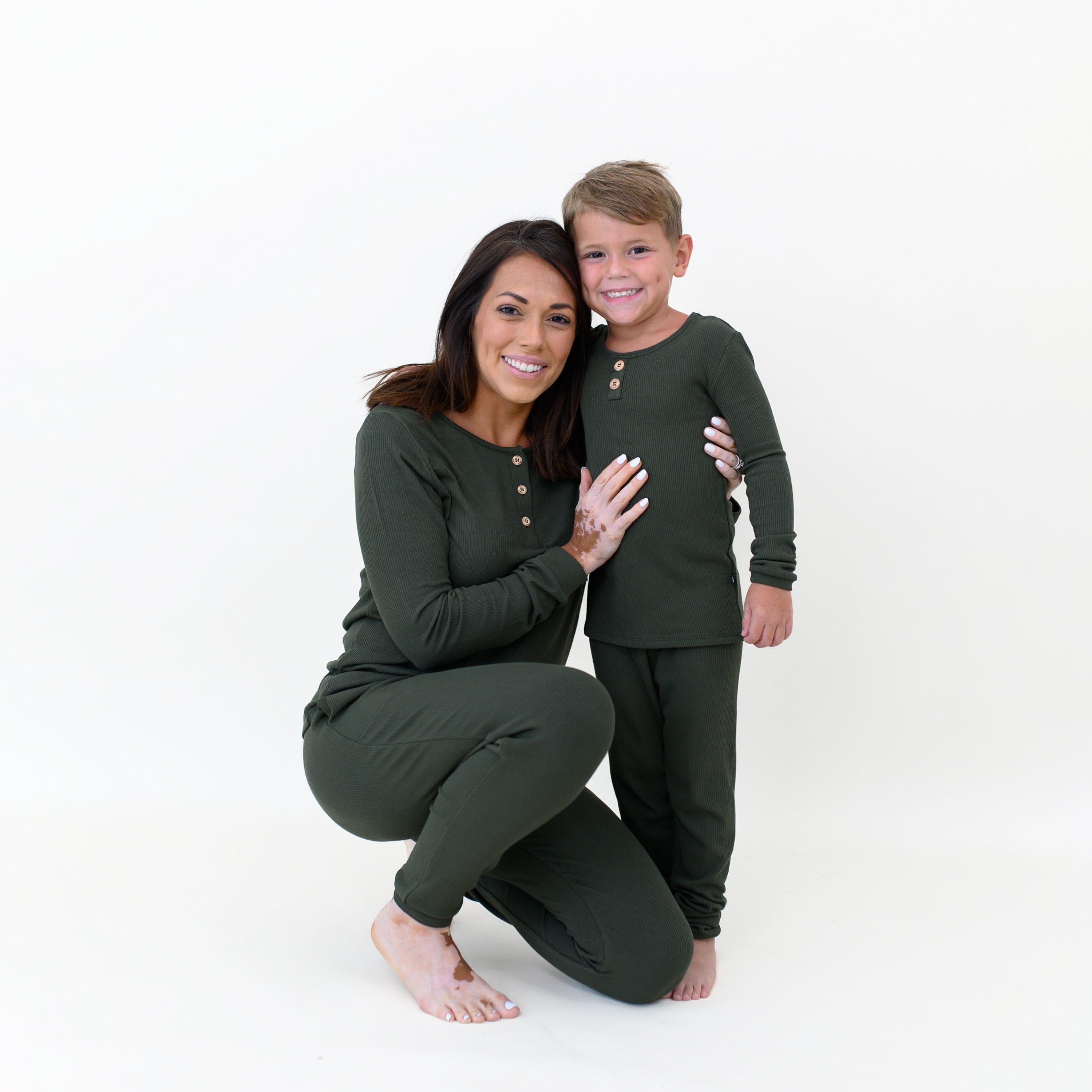 Mother kneeling beside her son with her arms around him matching him wearing the Women’s Ribbed Henley Set in Fir