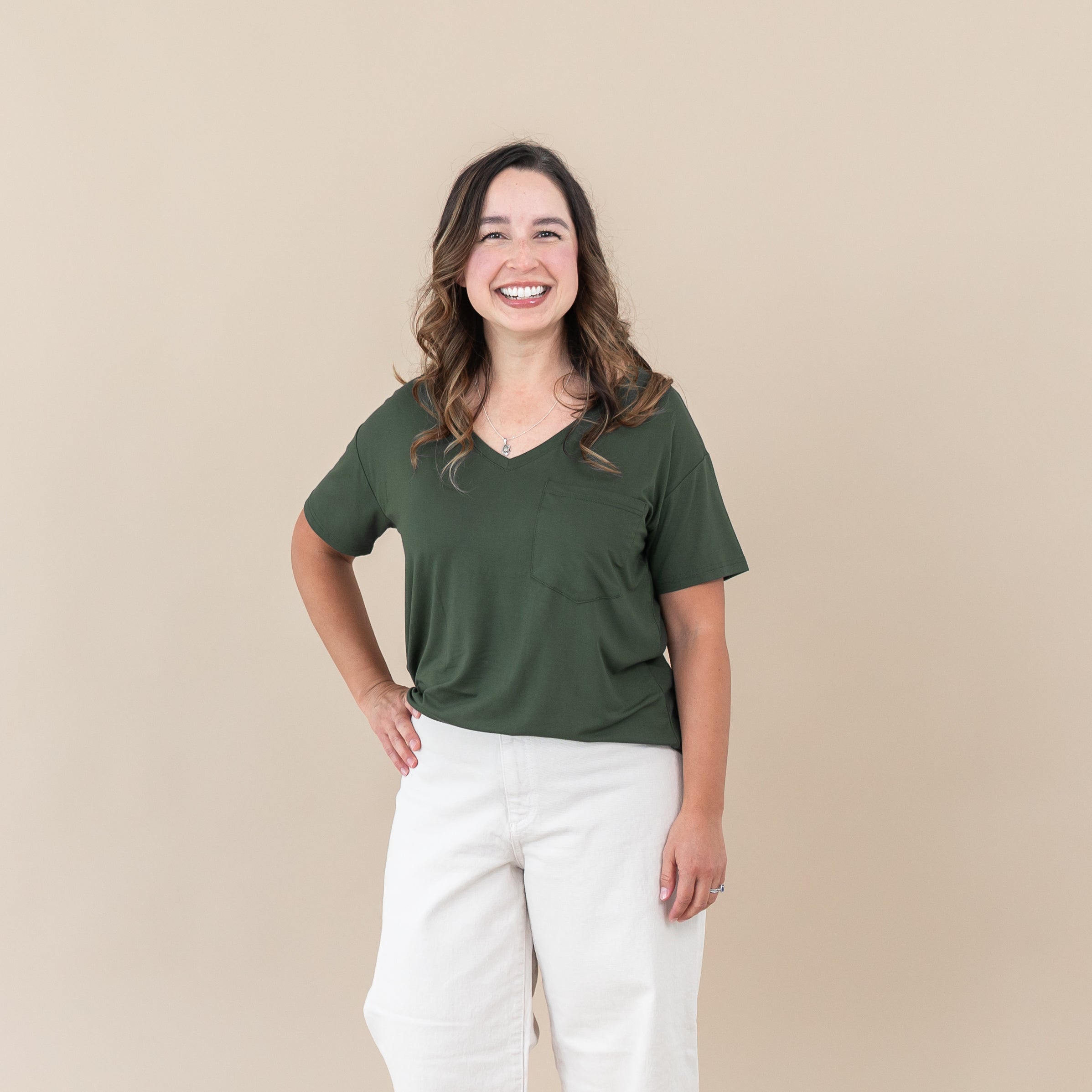 Woman wearing Women’s Relaxed Fit V-Neck in Fir and white pants against a beige background