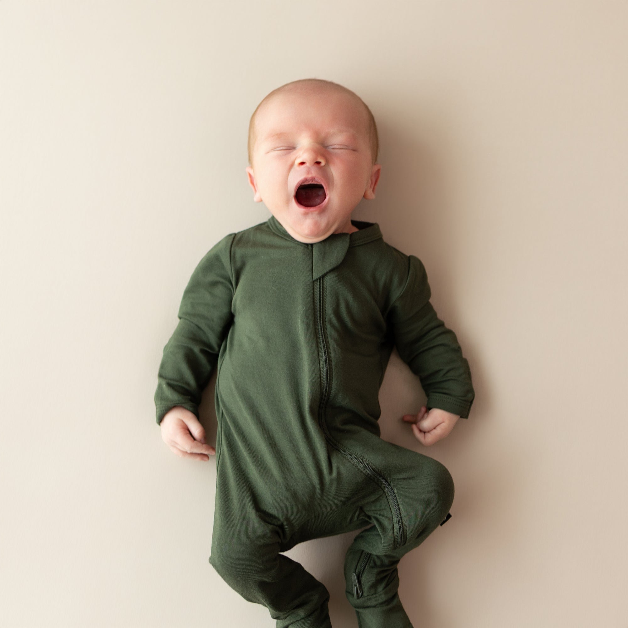Baby in a green onesie yawning on a beige background
