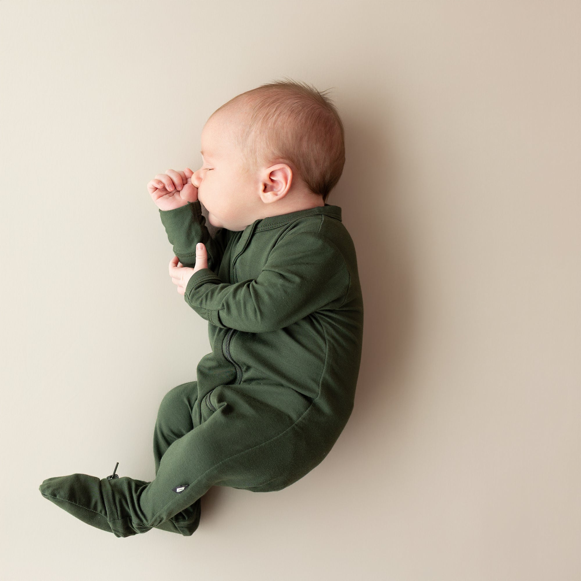 Baby in a green onesie lying on a beige surface