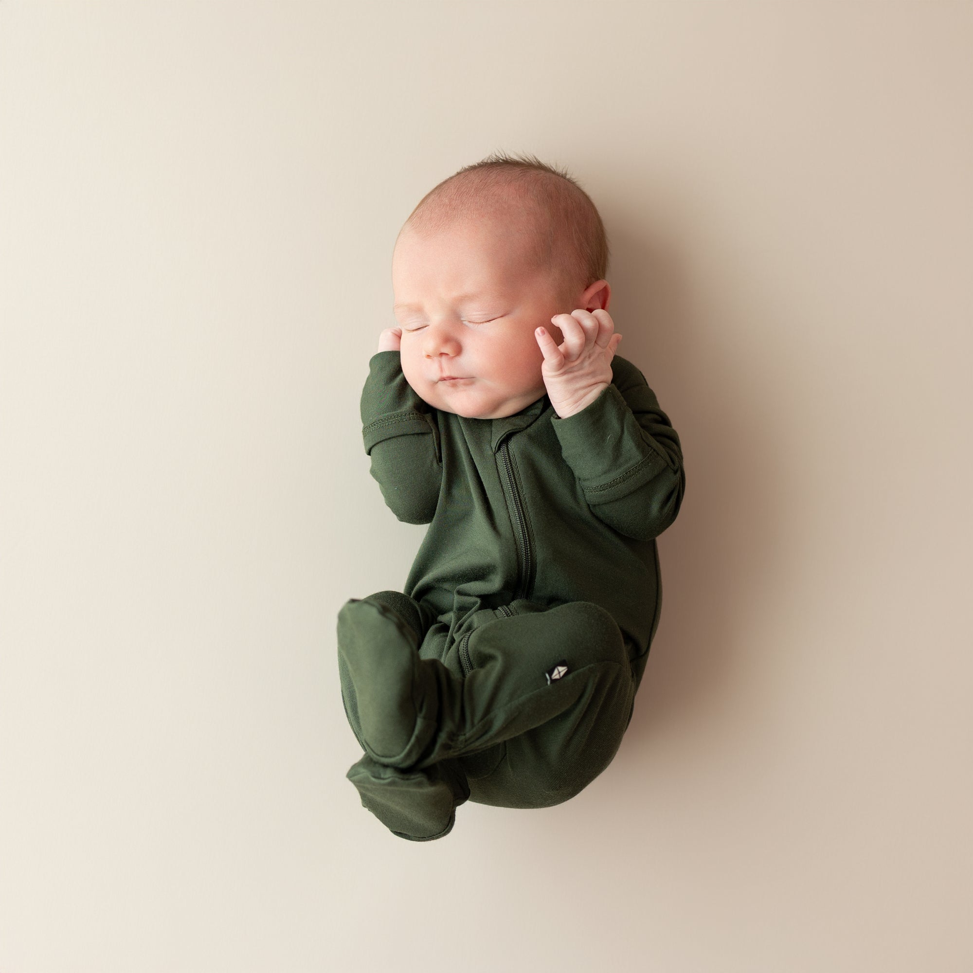 Newborn baby wearing a green onesie against a beige background