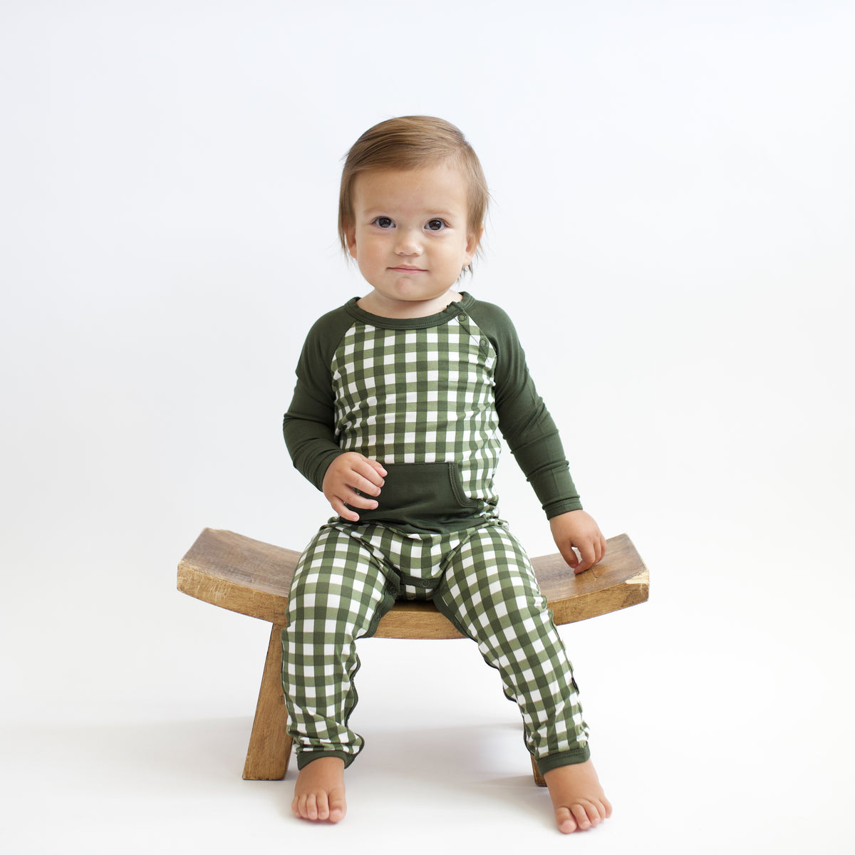 Toddler boy sitting on a wood stool wearing the Longall in Gingham Fir