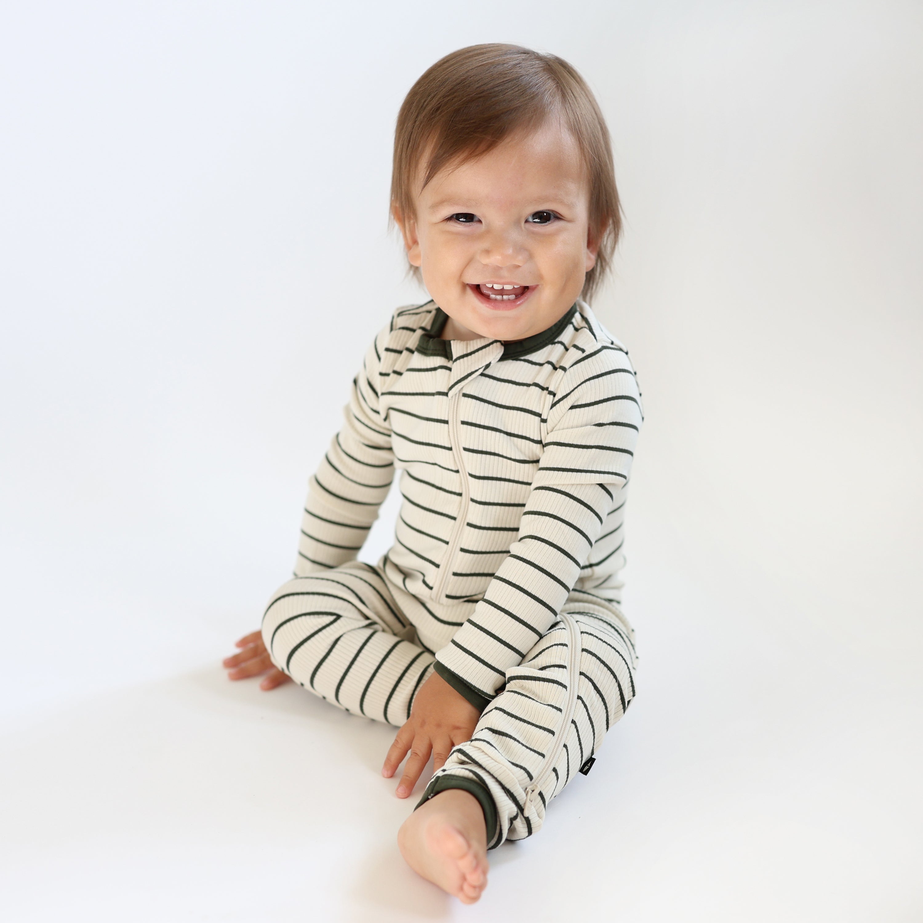 Young toddler sitting on the floor wearing the Ribbed Zipper Romper in Fir Stripe