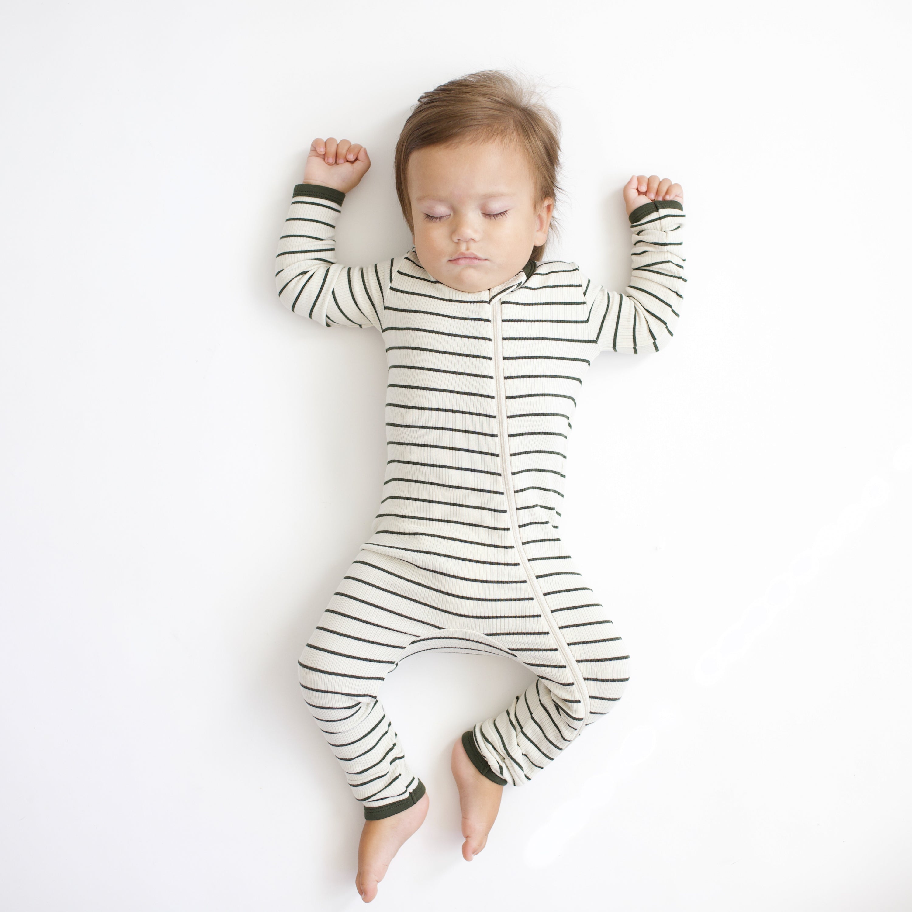 Sleeping toddler laying on a white background wearing the Ribbed Zipper Romper in Fir Stripe
