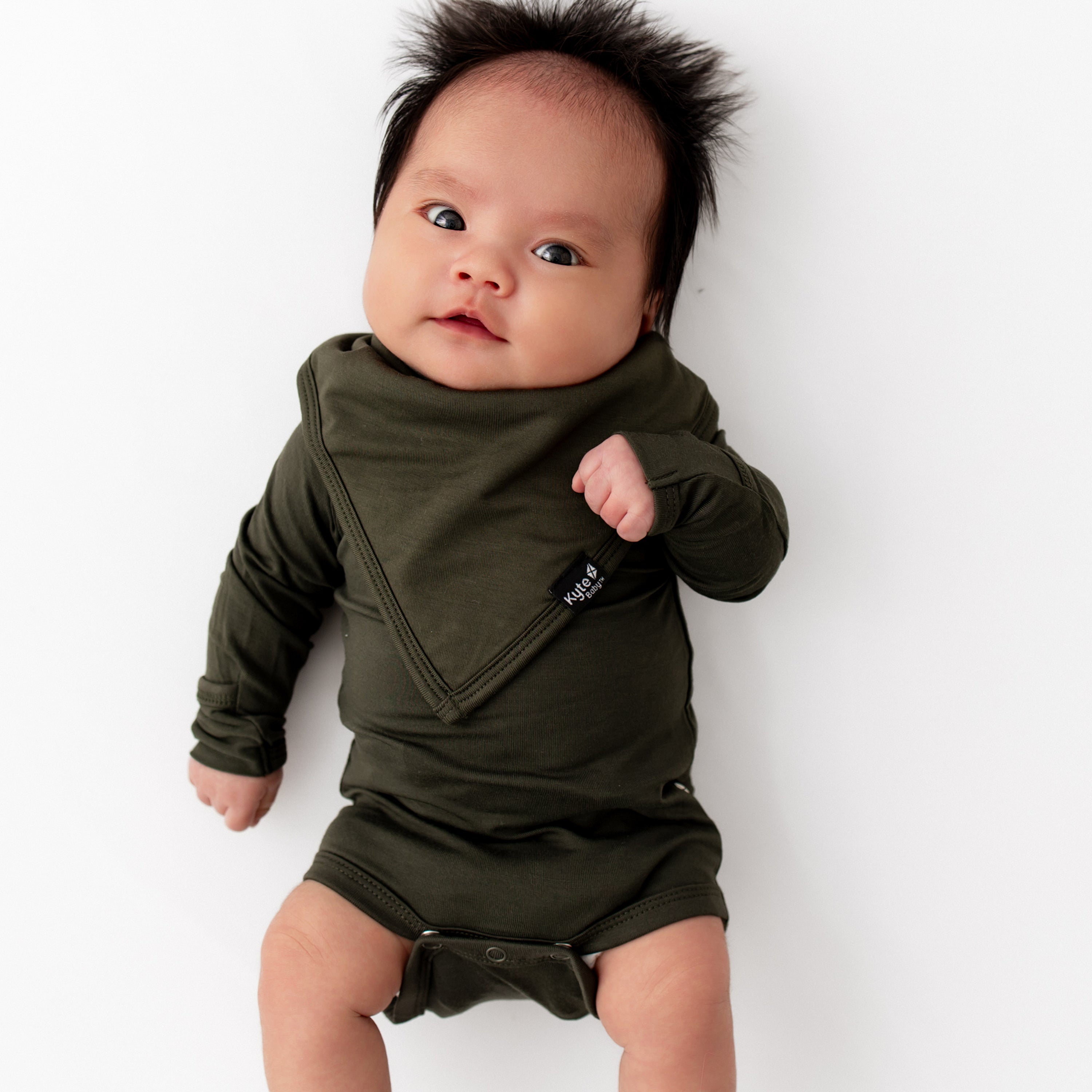 Baby wearing a dark green outfit and matching bib on white backdrop