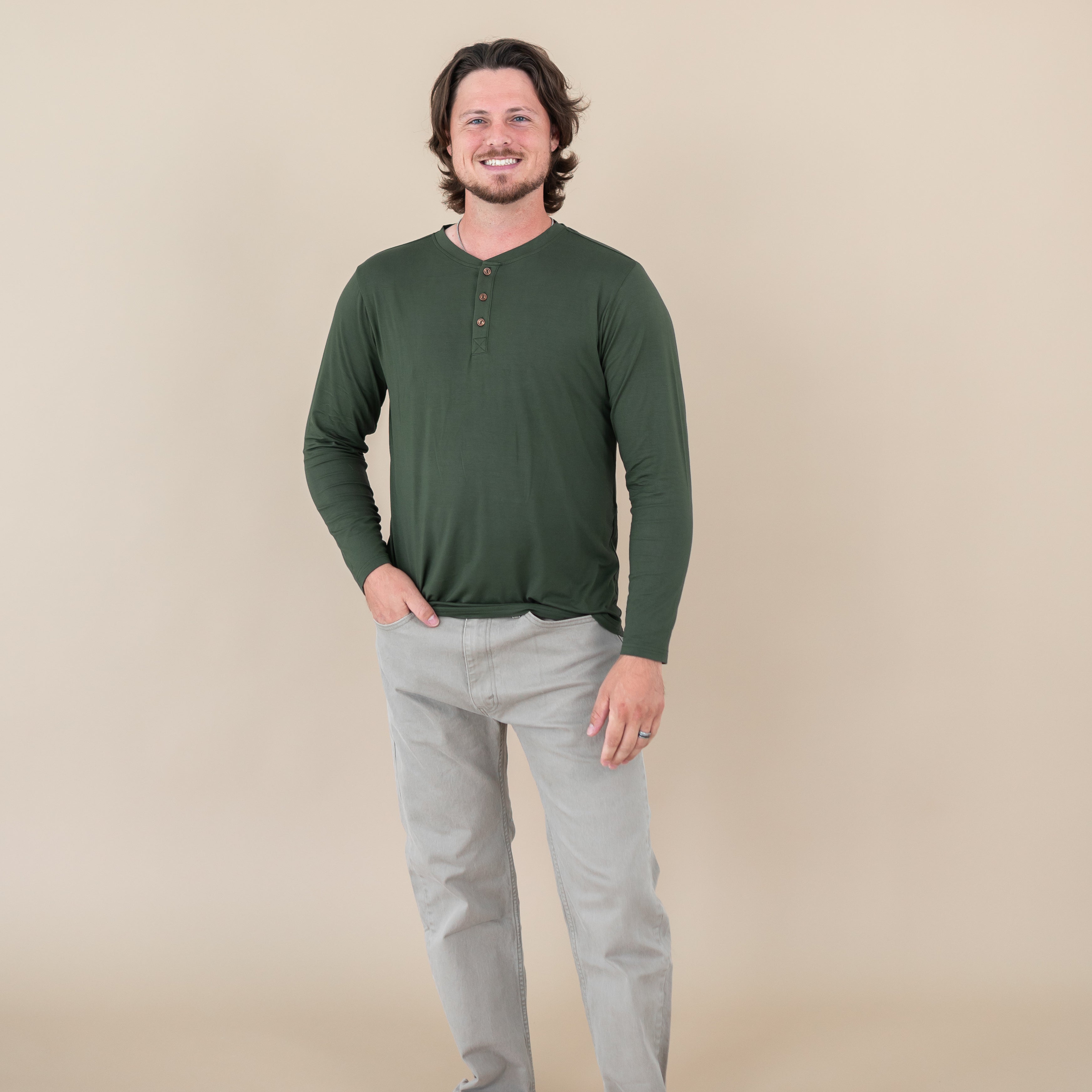Man wearing a Men's Long Sleeve Henley Top in Fir and light gray pants against a beige background