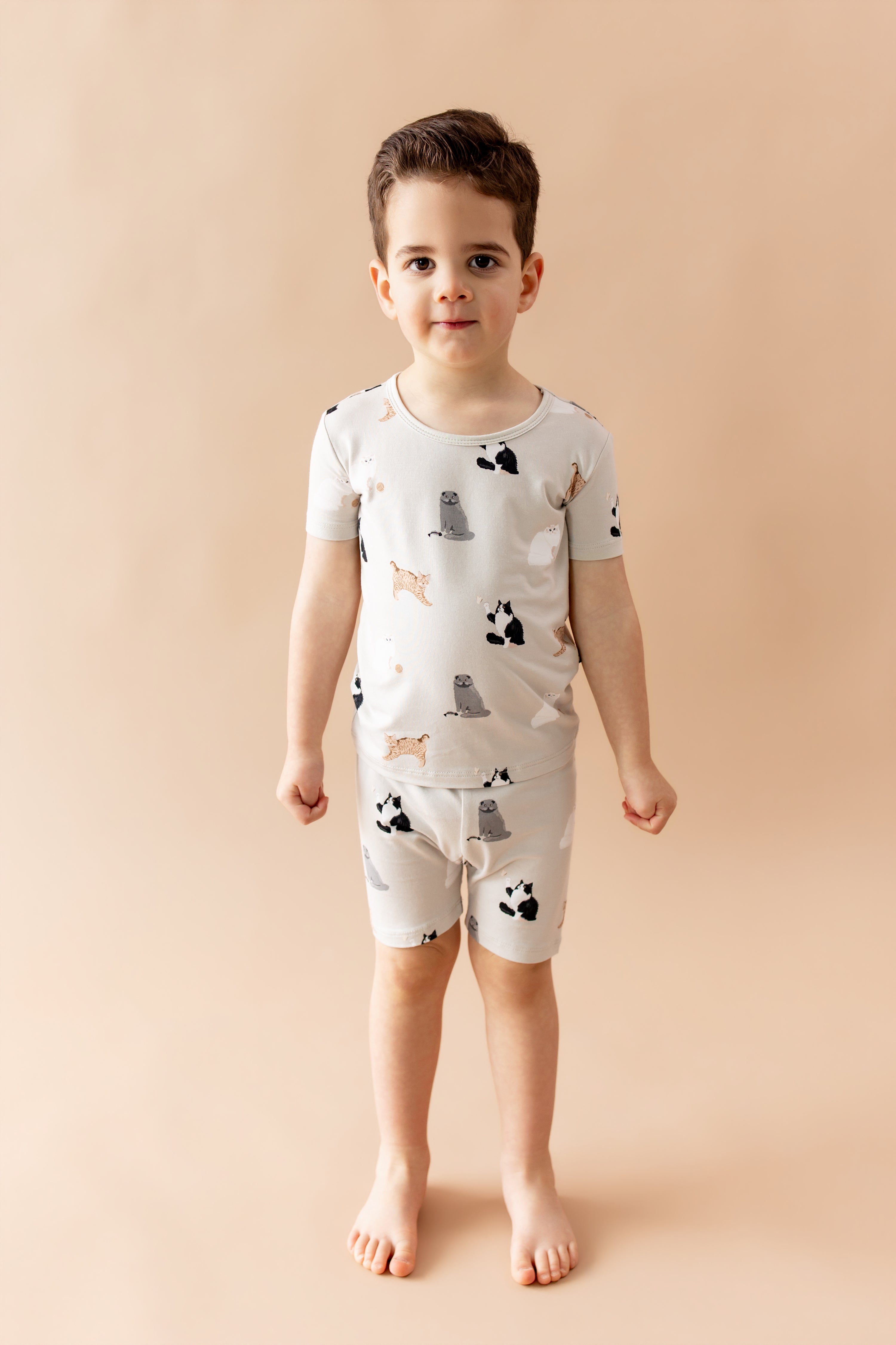 Young boy standing in front of a light beige background wearing the Short Sleeve Pajamas in Fluffy Cat