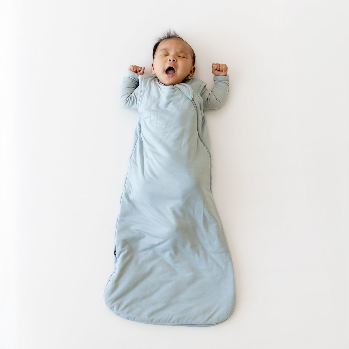 Baby yawning in a light blue sleep bag