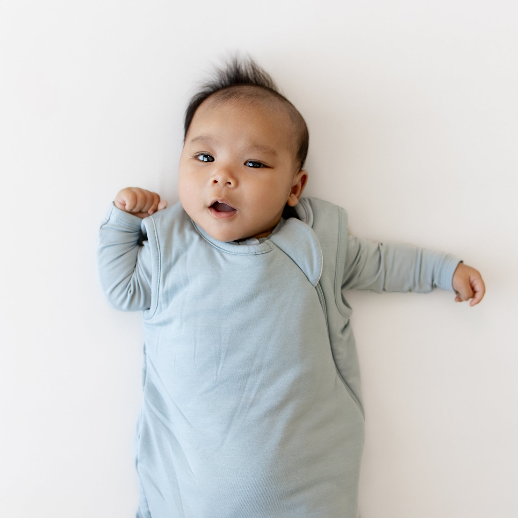 Baby wearing a light blue sleep bag on a white background