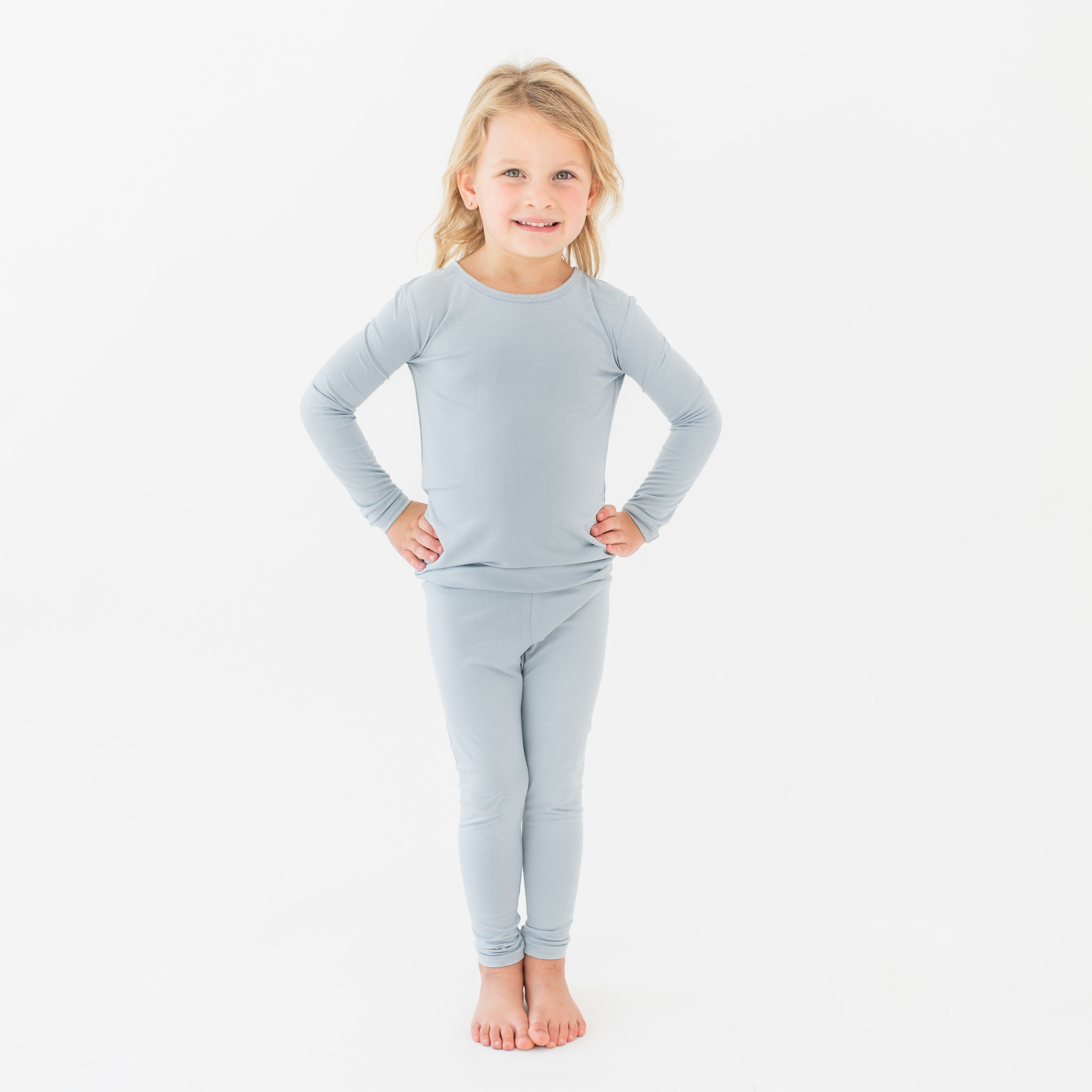 Young girl standing with both hands on her hips wearing the Long Sleeve Pajamas in Fog in front of a white background