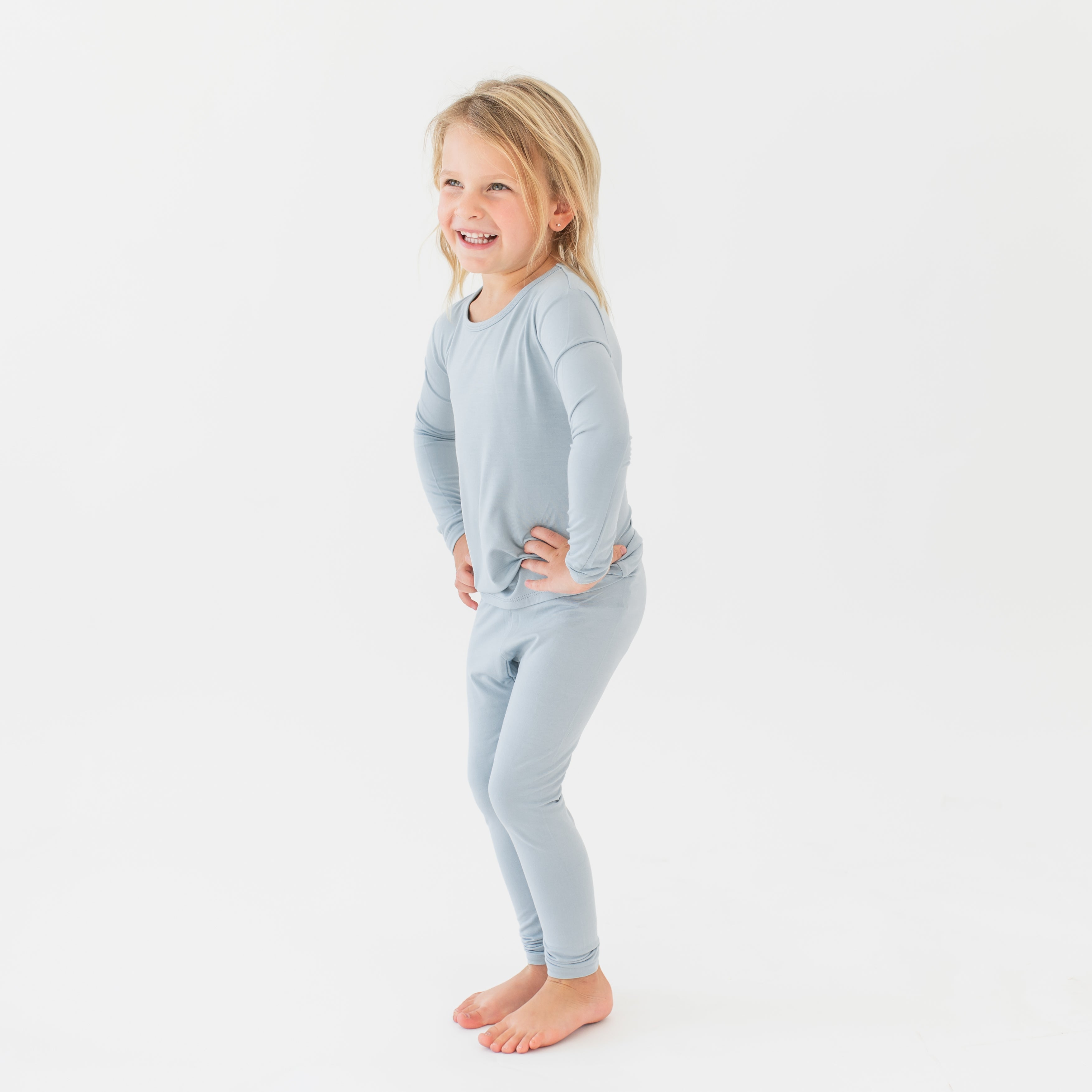 Young girl standing with her hands on her hips wearing the Long Sleeve Pajamas in Fog in front of a white background