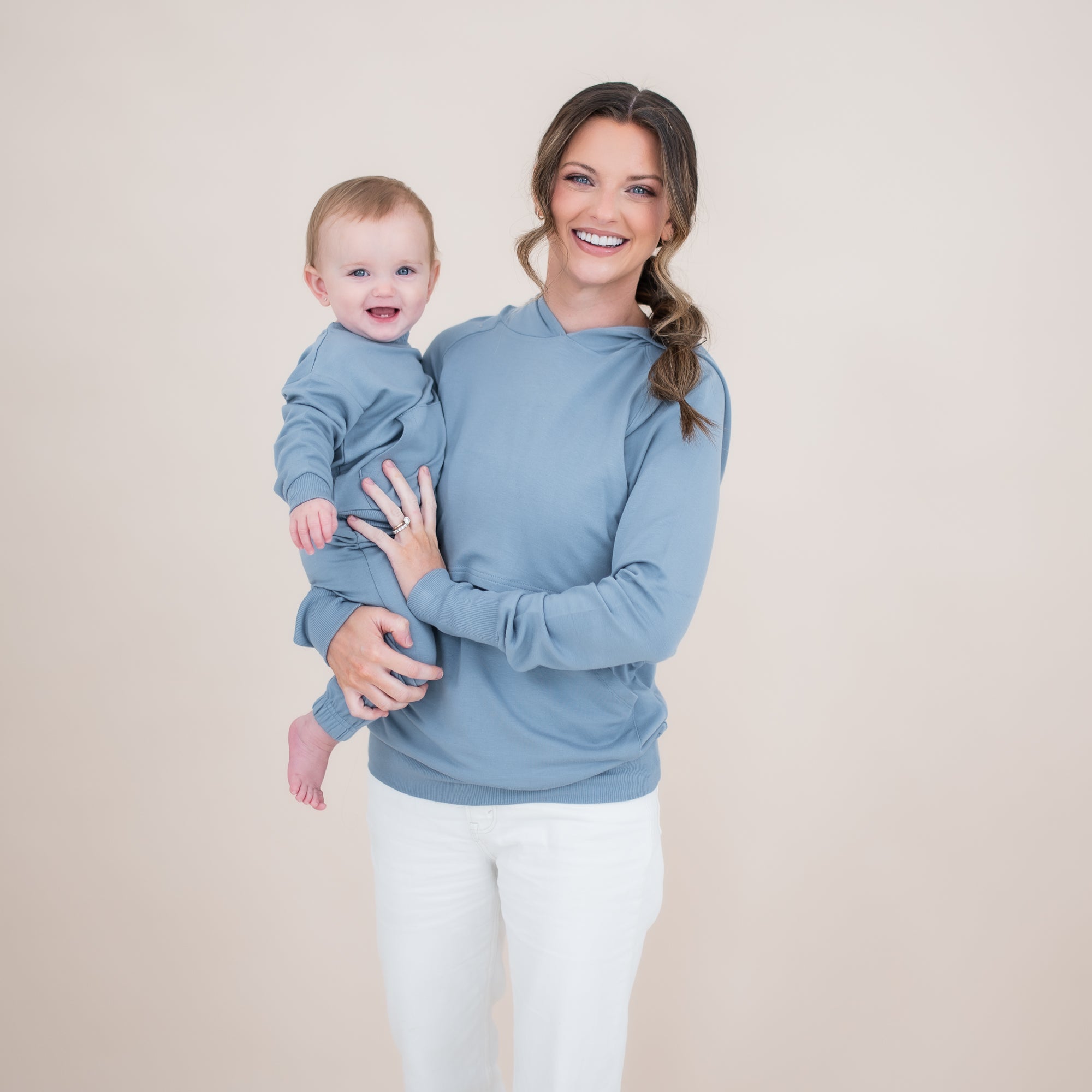 Mother wearing the Women's French Terry Nursing Hoodie in Slate and white pants holding her infant who is in a matching french terry jogger set
