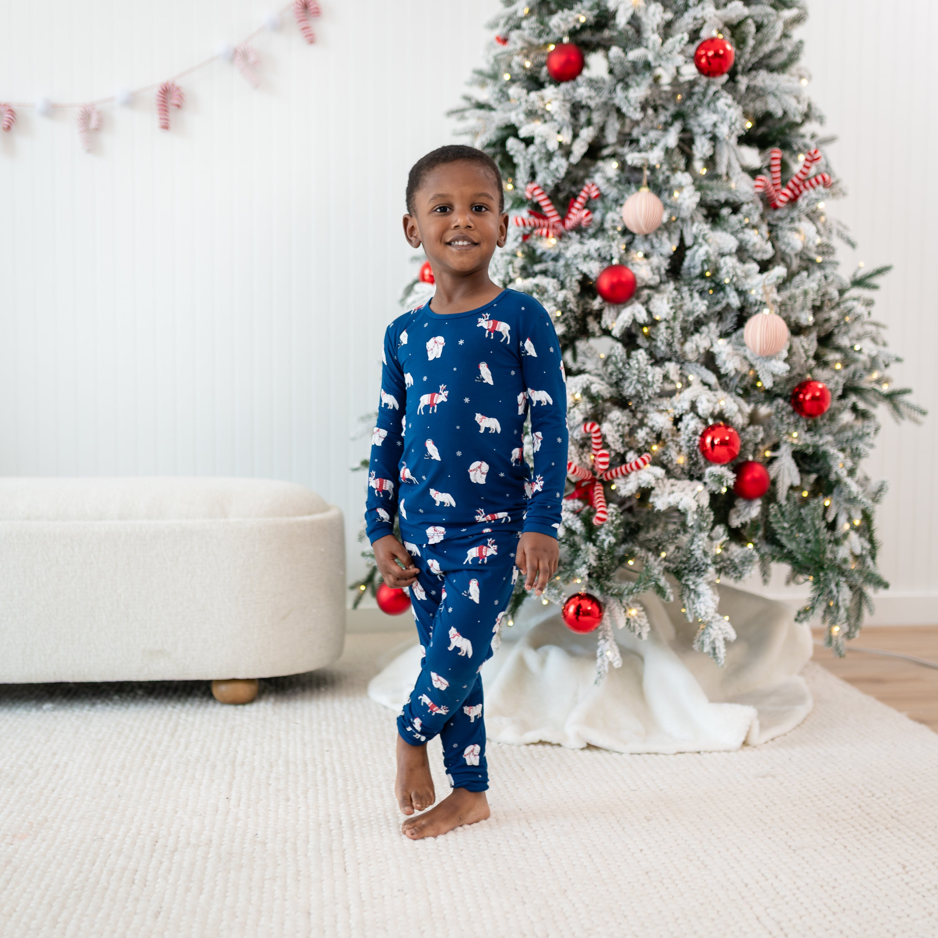Young boy standing in front of a decorated Christmas tree wearing the Long Sleeve Pajamas in Frosty Friends