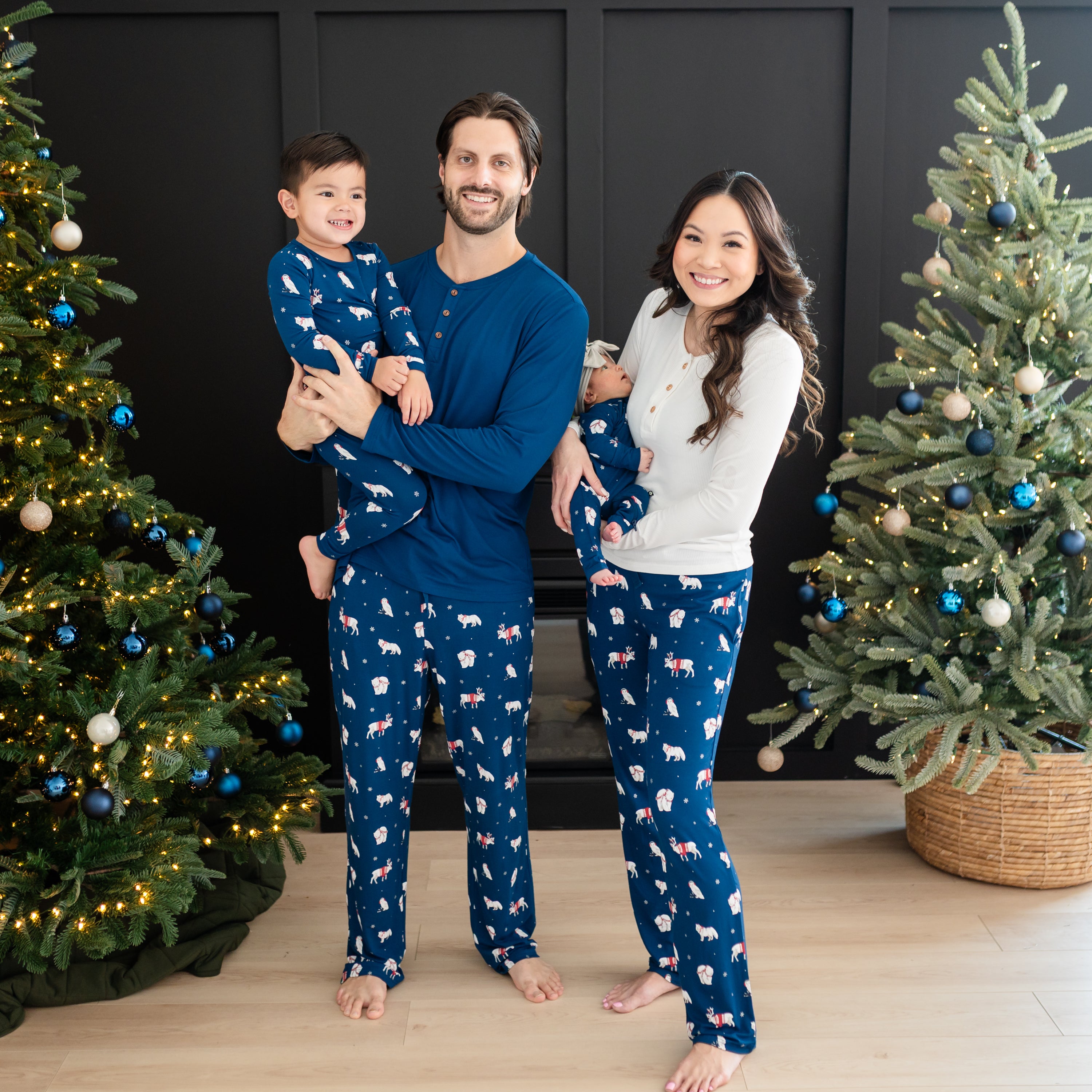 Family of four wearing various items in the holiday print Frosty Friends standing between two decorated Christmas Trees