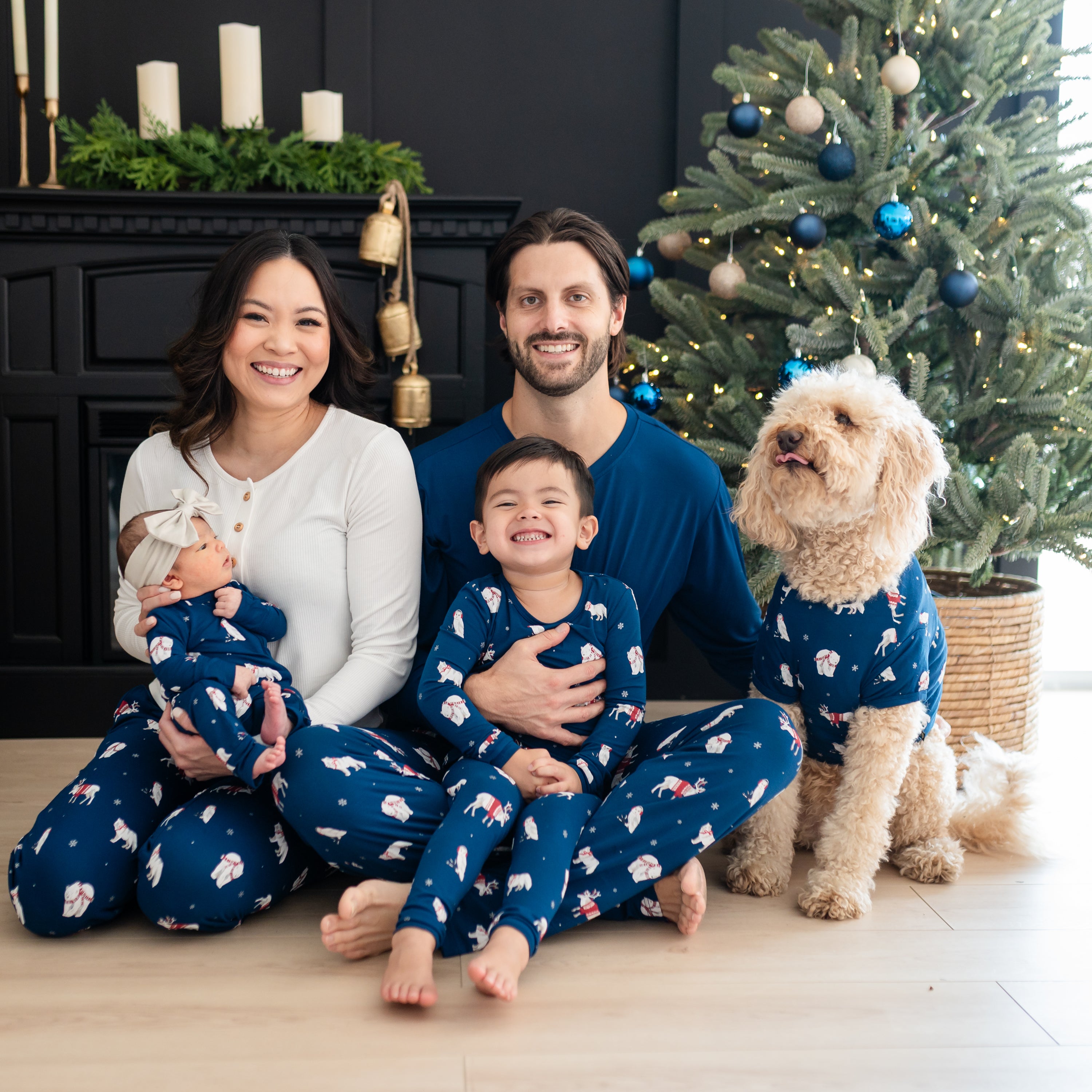Family of four sitting on the floor matching in various Frosty Friends items with a medium sized dog sitting beside them wearing the dog tee