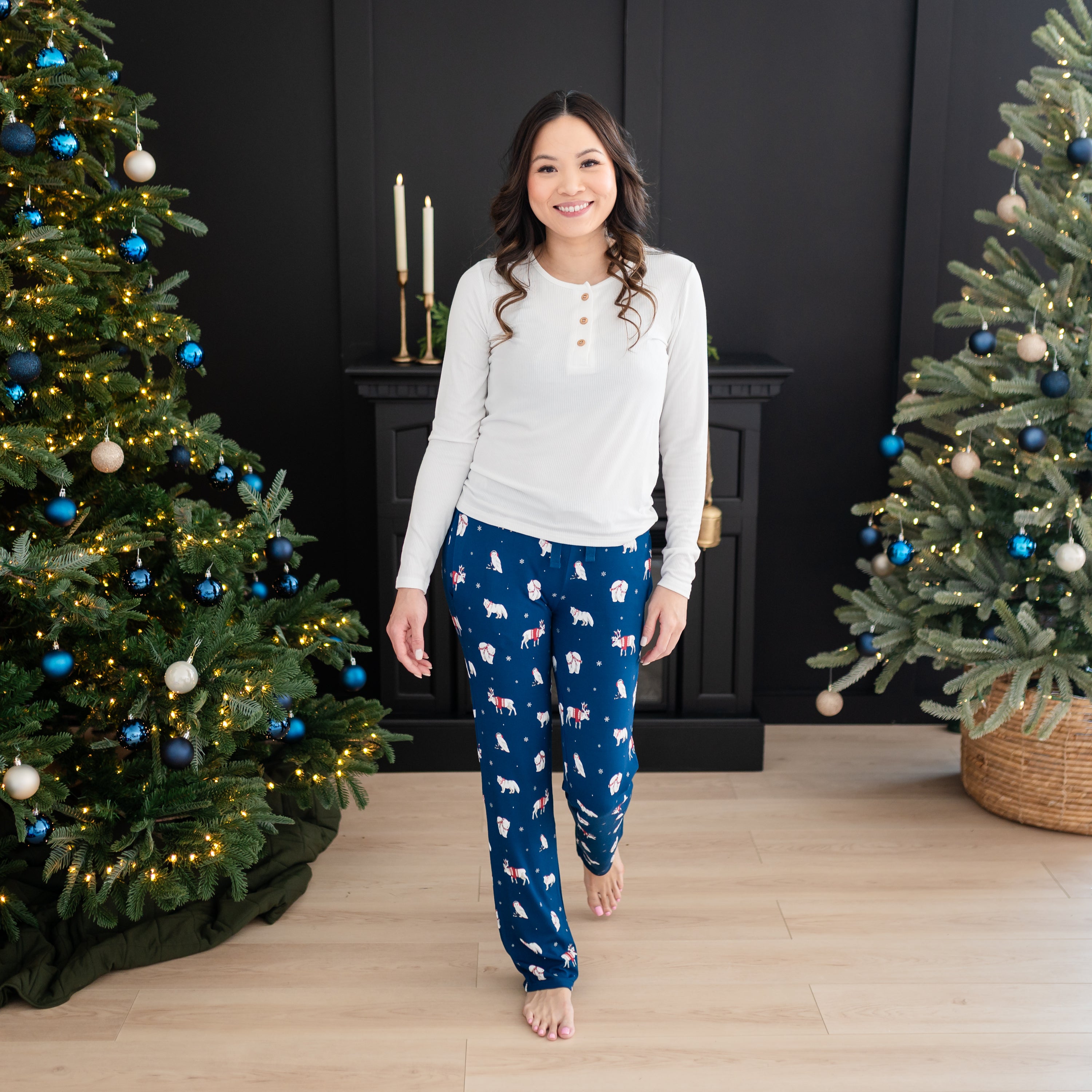 Smiling female walking wearing the Women's Lounge Pants in Frosty Friends with a white colored henley with two decorated Christmas trees in the background