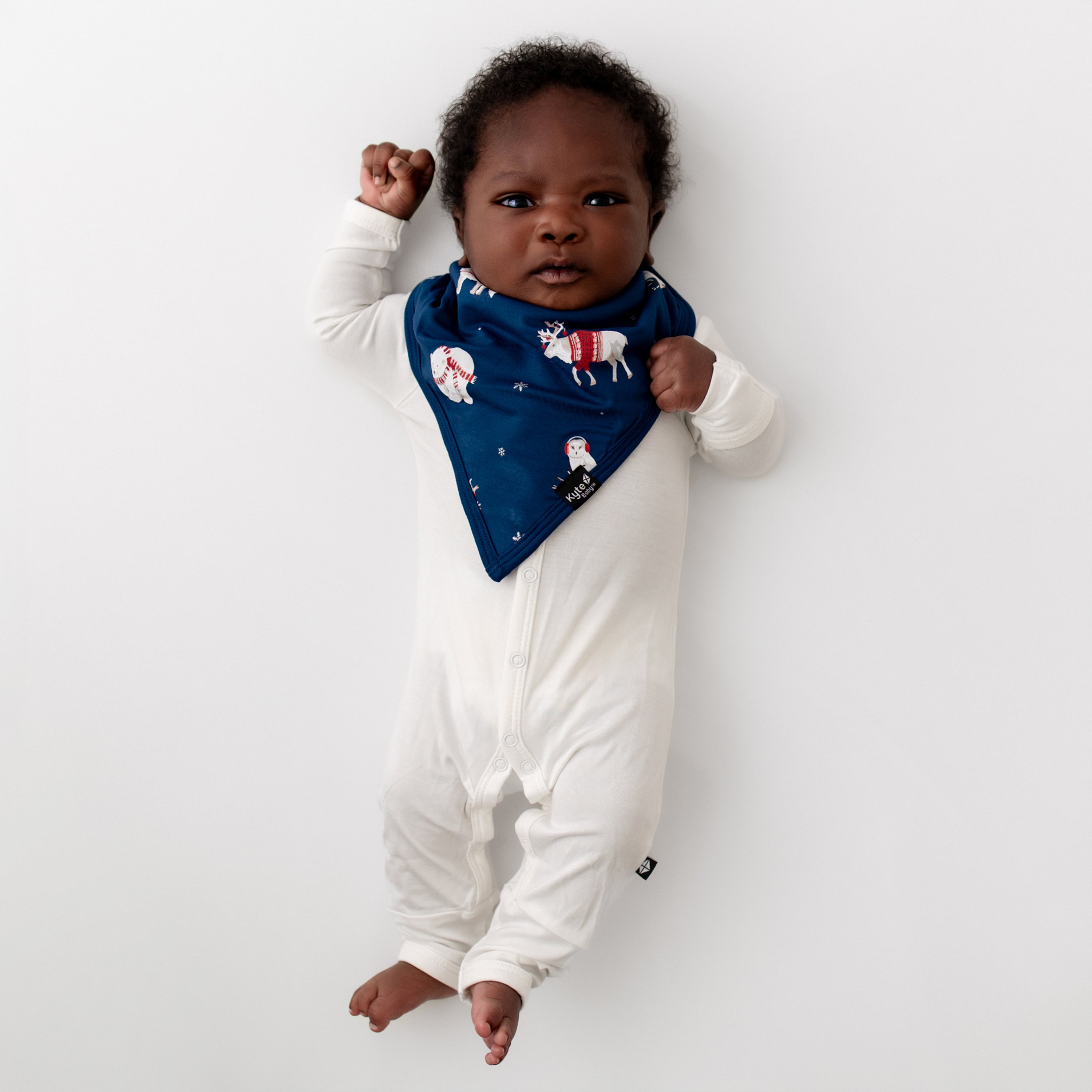 Newborn baby laying on a white blanket wearing the Bib in Frosty Friends and Cloud Snap Romper