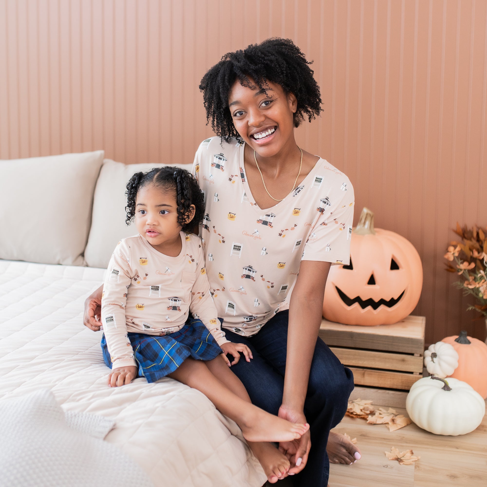 Mother and daughter sitting on a bed matching in gilmore girls tees