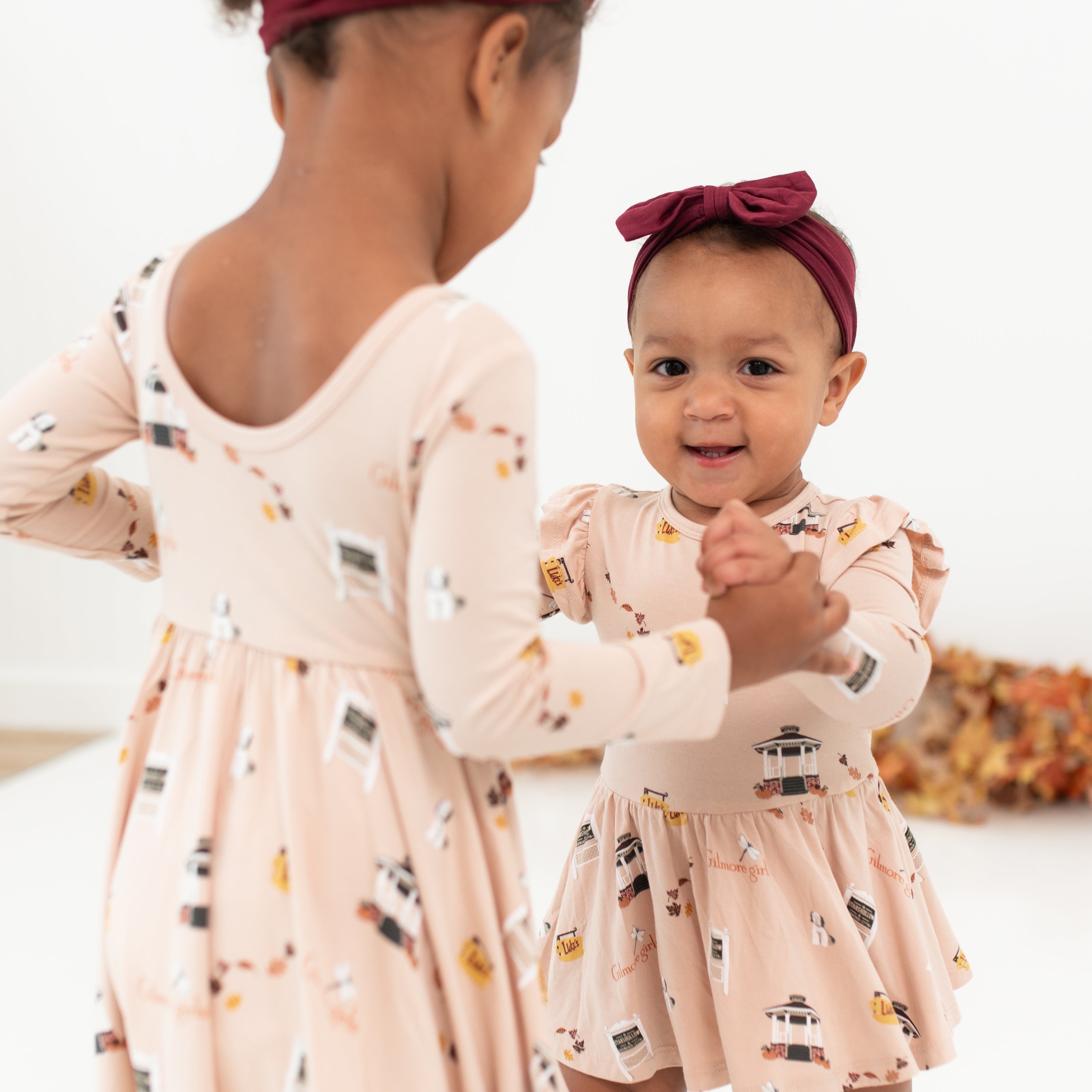 Two sisters standing holding hands matching in Gilmore Girl dresses with the emphasis of the ballerina back on the Long Sleeve Twirl Dress in Gilmore Girls