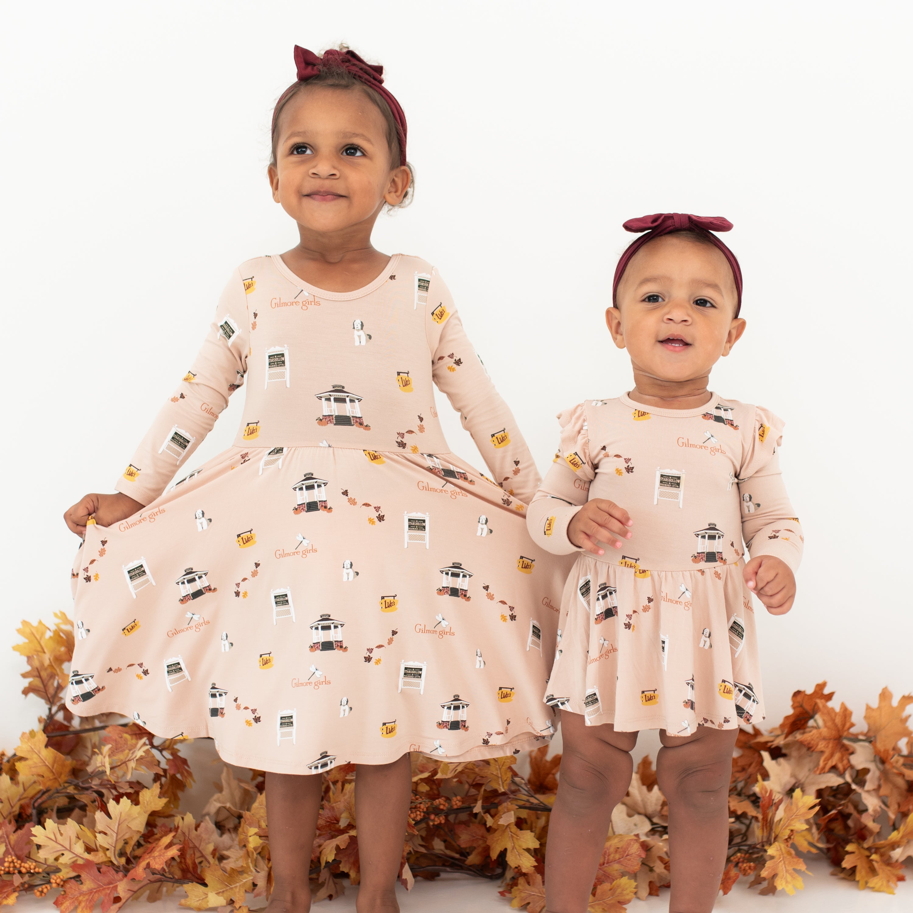 Two sisters standing side by side wearing the Long Sleeve Twirl Dress and Twirl bodysuit dress in Gilmore Girls. Oldest sister is wearing the twirl dress and extending the skirt fabric out with both hands