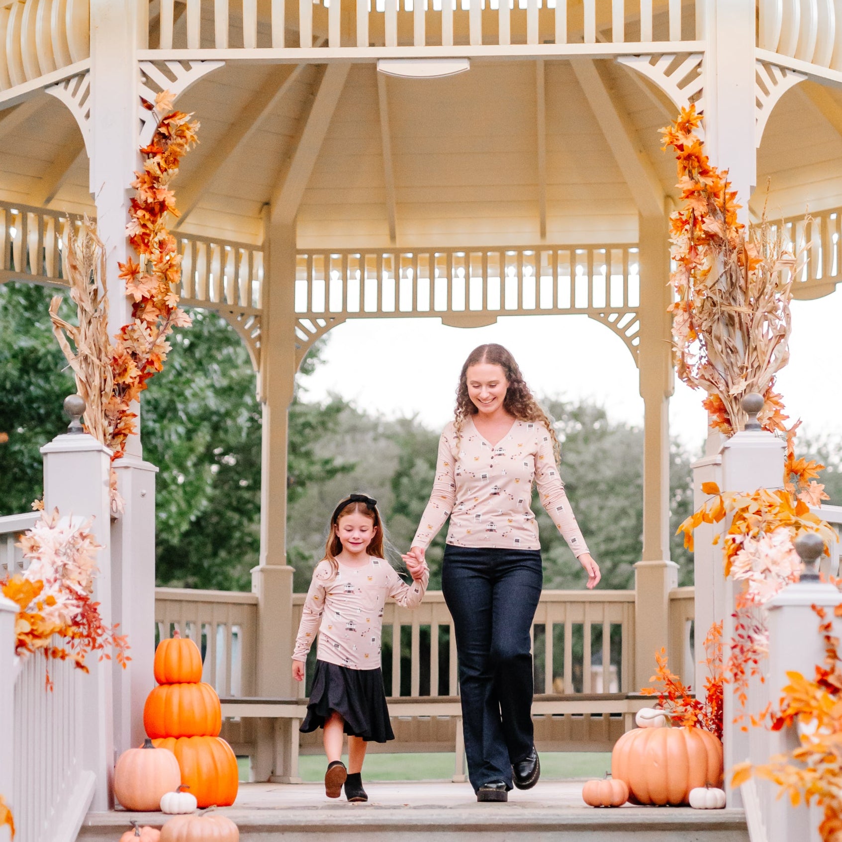 Mother and daughter holding hands wearing Gilmore Girl tops walking through the entrance of a gazebo with fall inspired decorations around them
