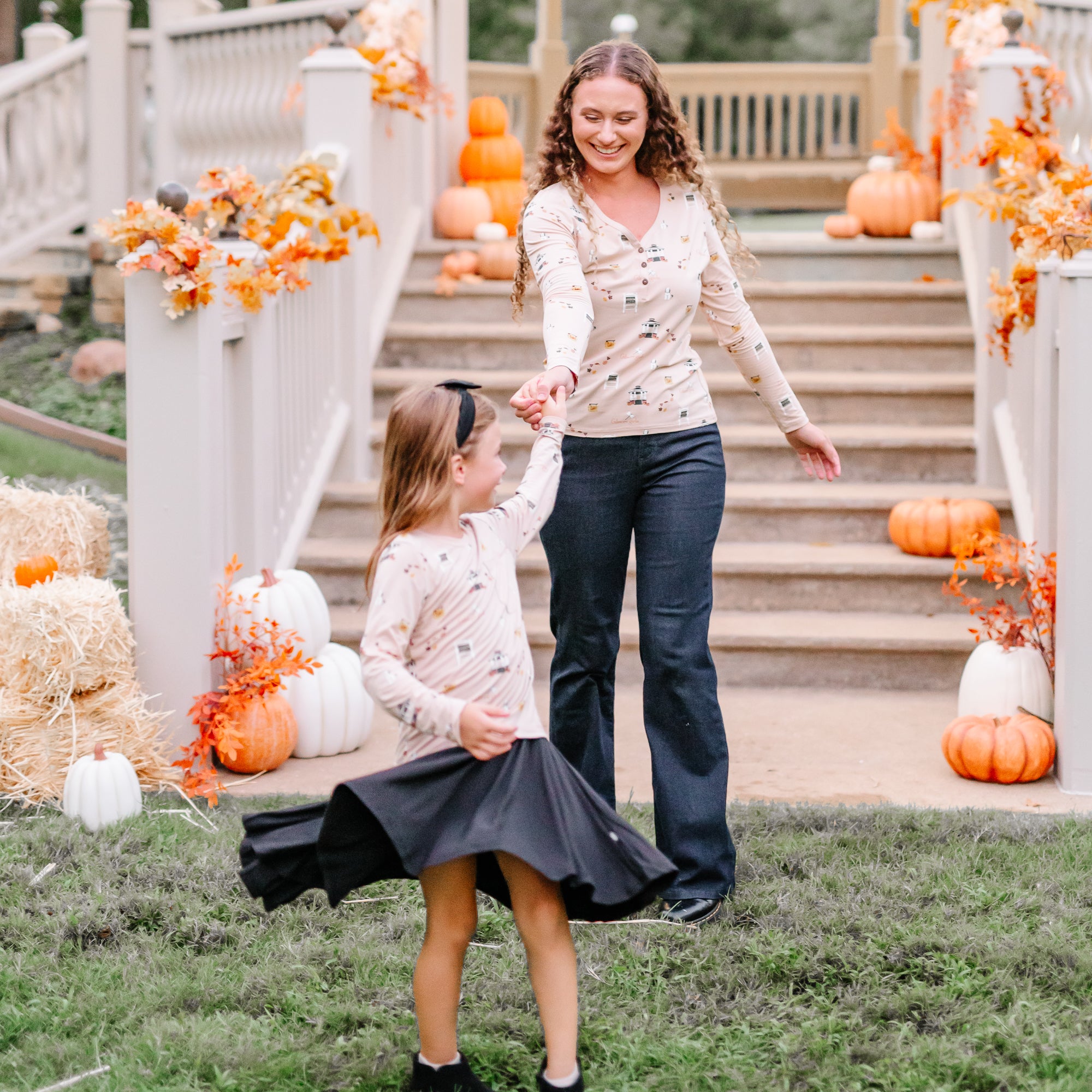 Mother holding daughters hand while daughter is twirling wearing a Gilmore Girls themed shirt and black twirl dress on underneath outside in front of a fall decorated gazebo