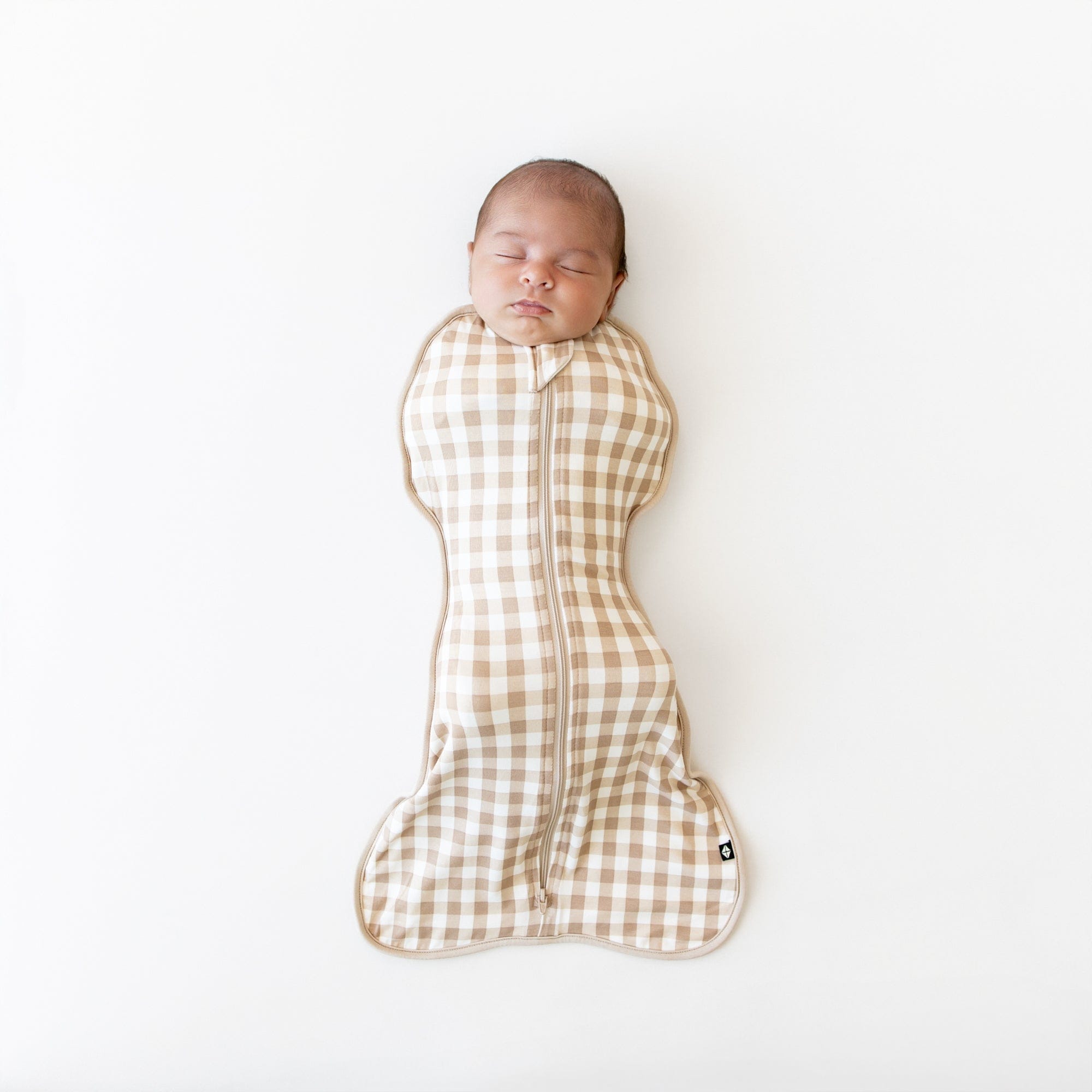 Newborn baby swaddled in a brown and white checkered swaddle bag on a white background