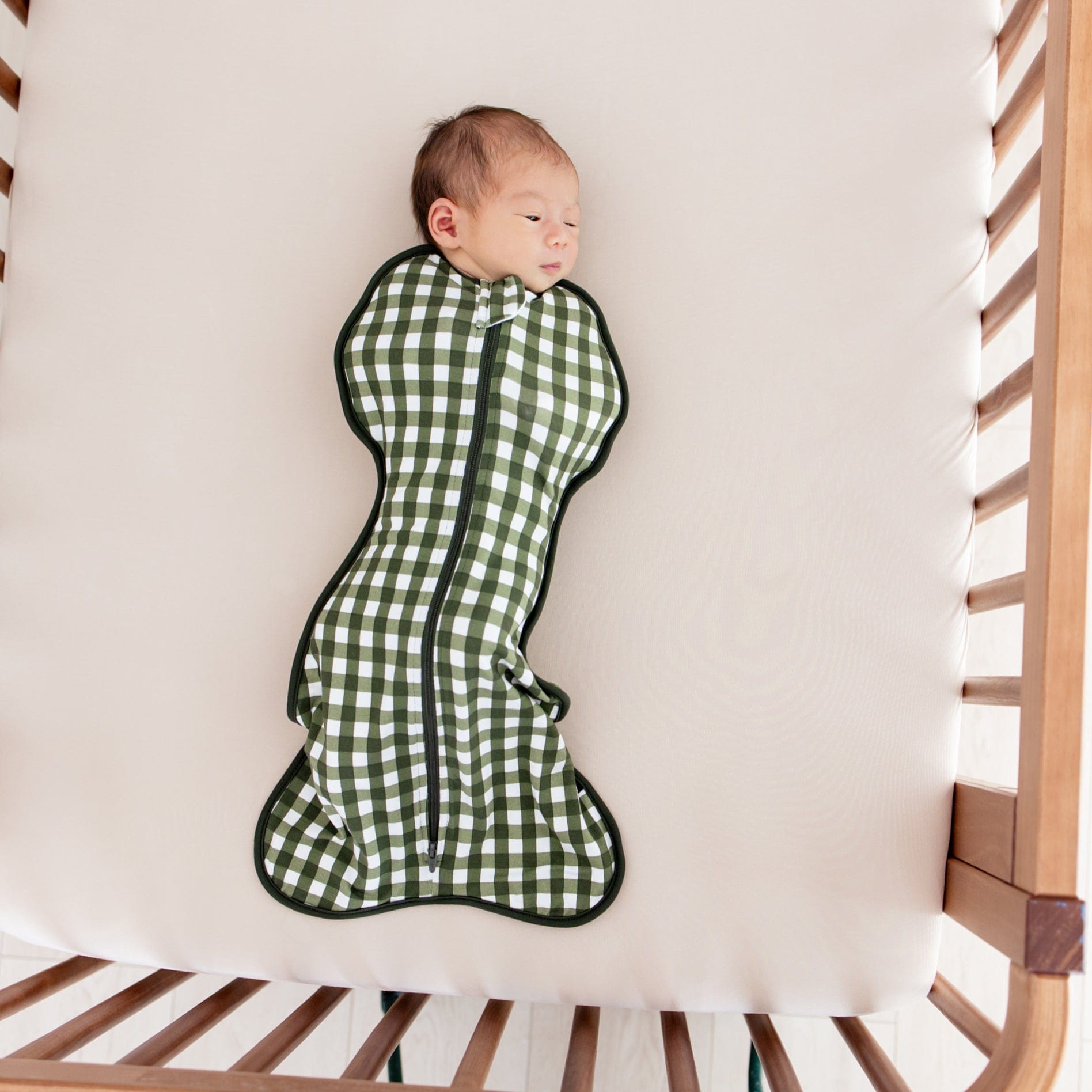 Baby in Swaddle Bag in Gingham Fir 0.5 laying in a crib