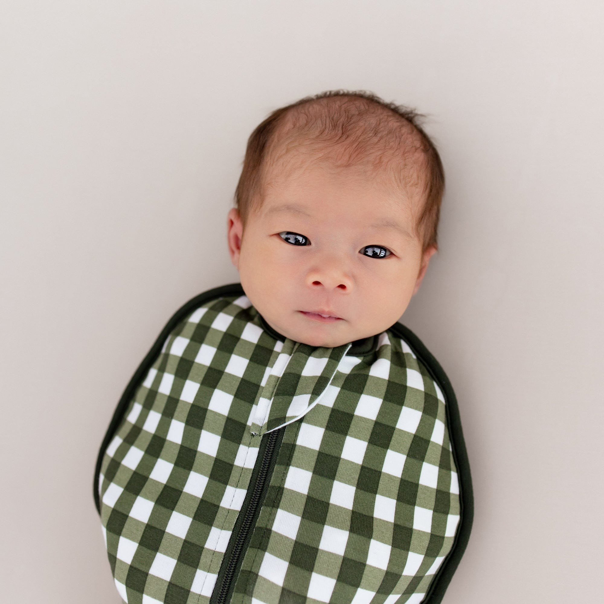 Close up on baby's face and top portion of the Swaddle Bag in Gingham Fir 0.5