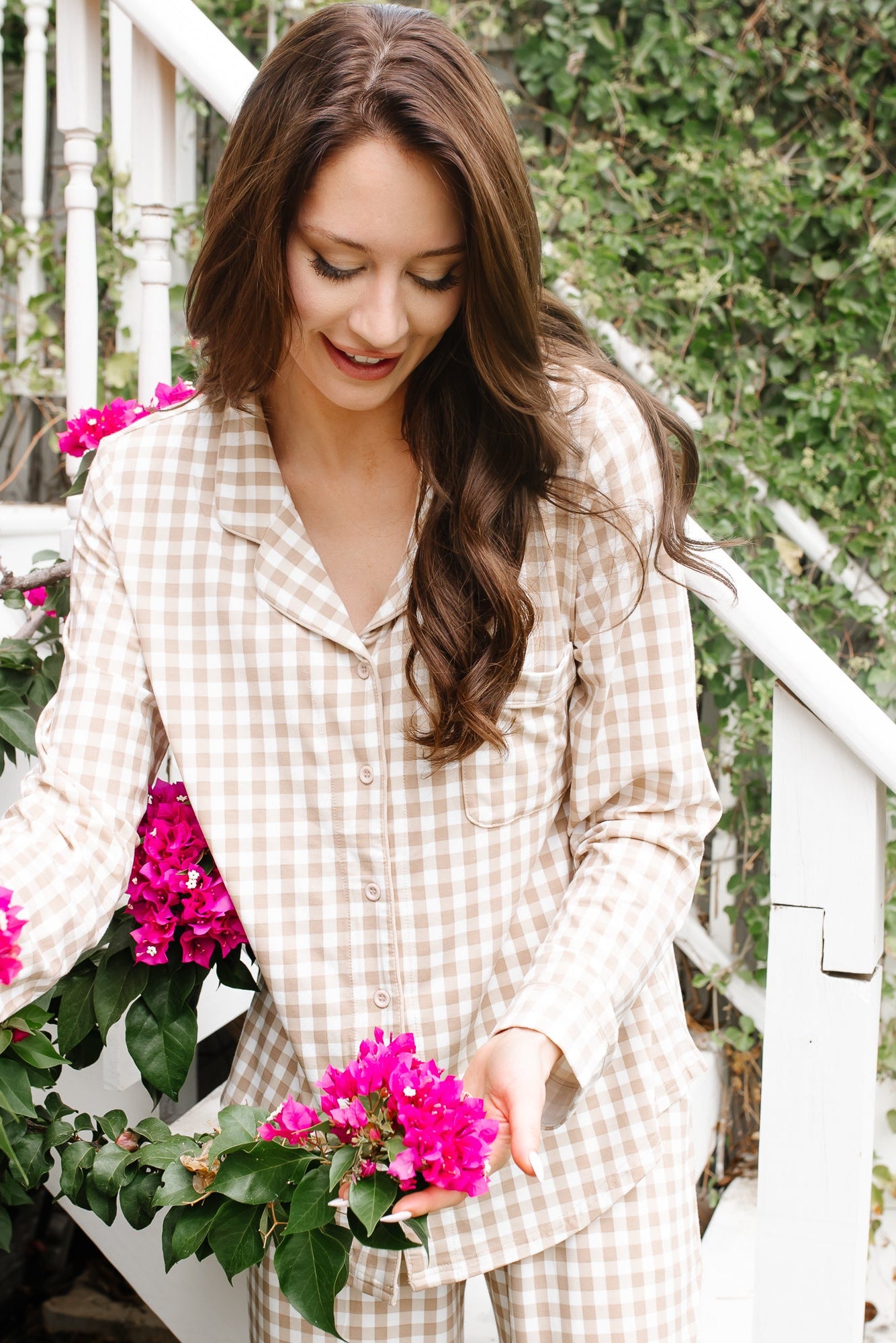 Close up of the Long-Sleeved Women's Pajama Set in Gingham Bisque shown on a female model standing on front steps holding pink colored flowers