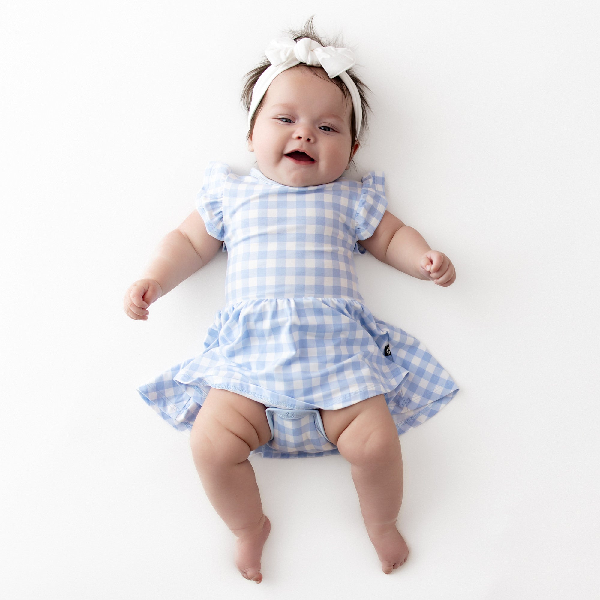 Infant wearing the Twirl Bodysuit Dress in Gingham Breeze with a knotted bow headband in cloud