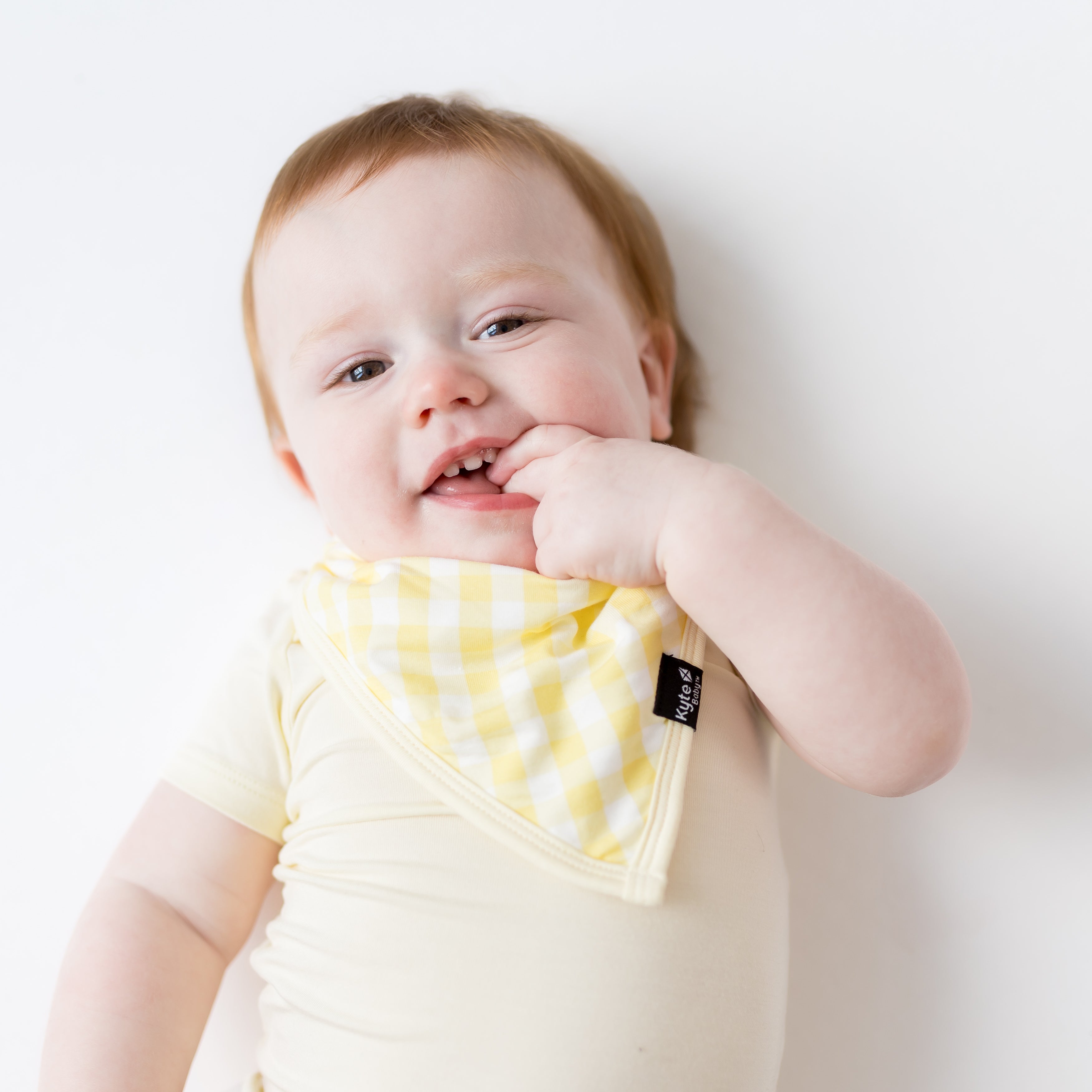 Young baby wearing the Bib in Gingham Chamomile with their fingers in their mouth