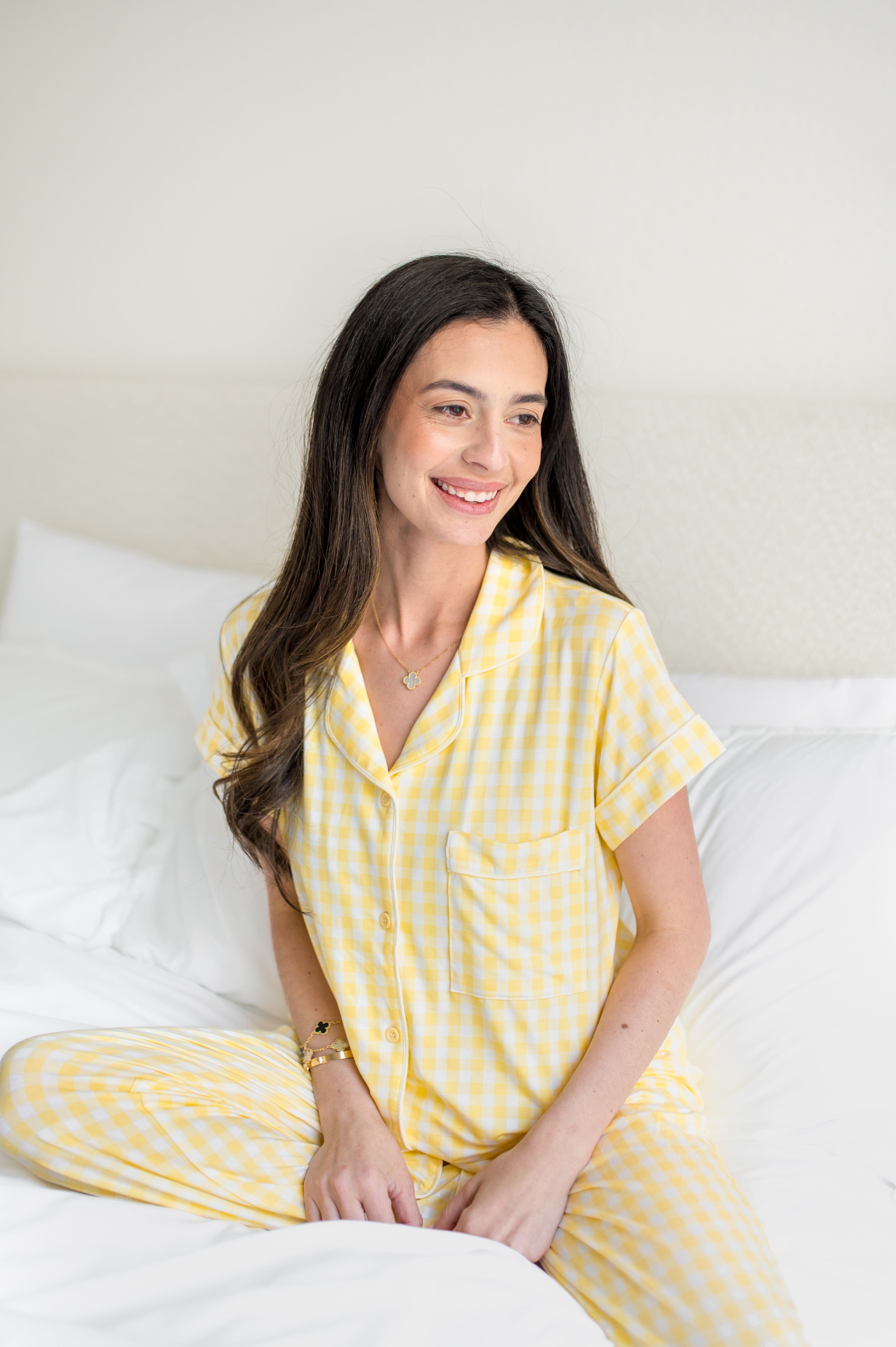 Smiling female sitting on a bed wearing the Women's Short Sleeve Cropped Pajama Set in Gingham Chamomile
