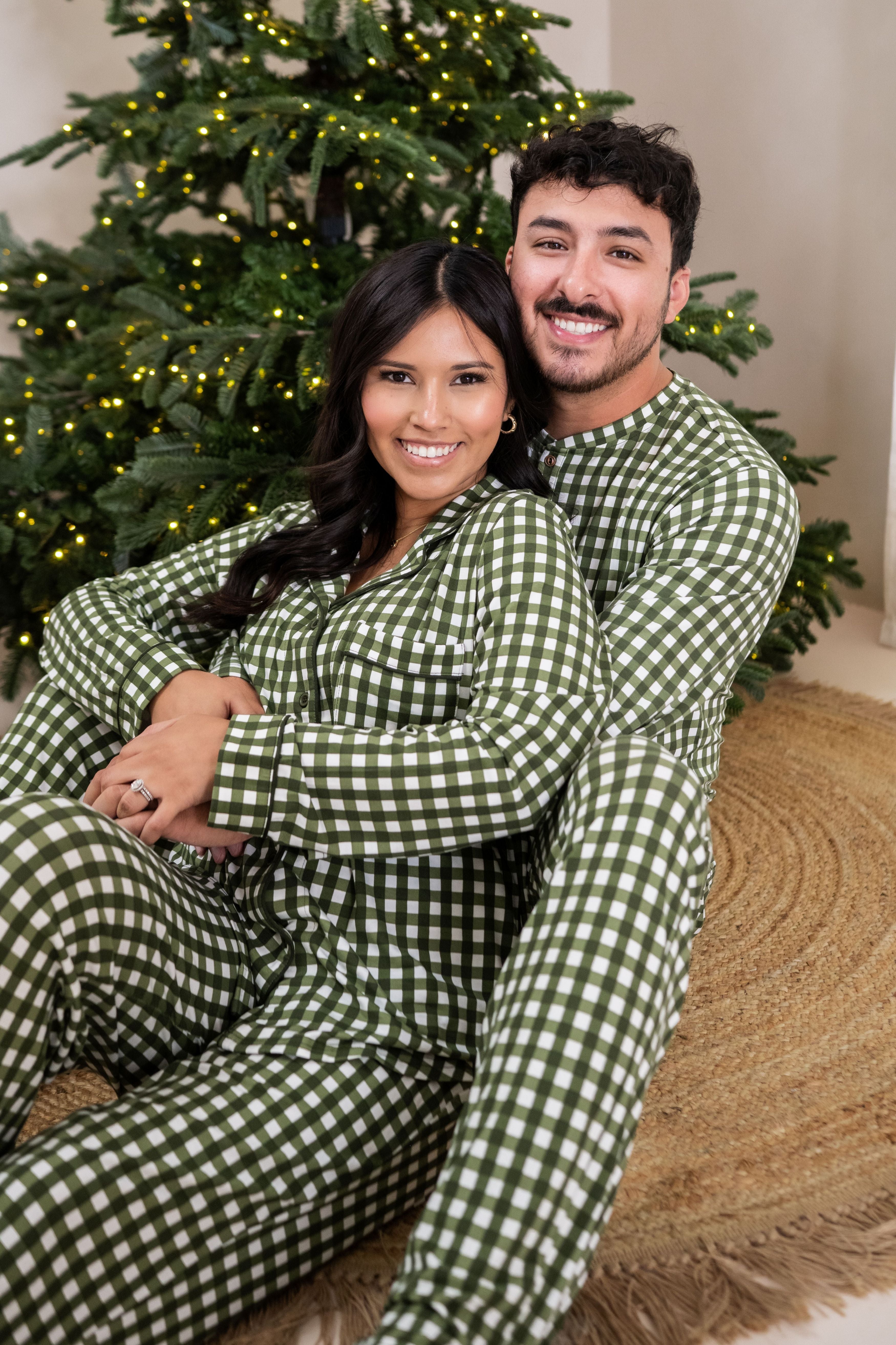 Husband and wife sitting on the floor wearing matching Pajama sets in Gingham Fir