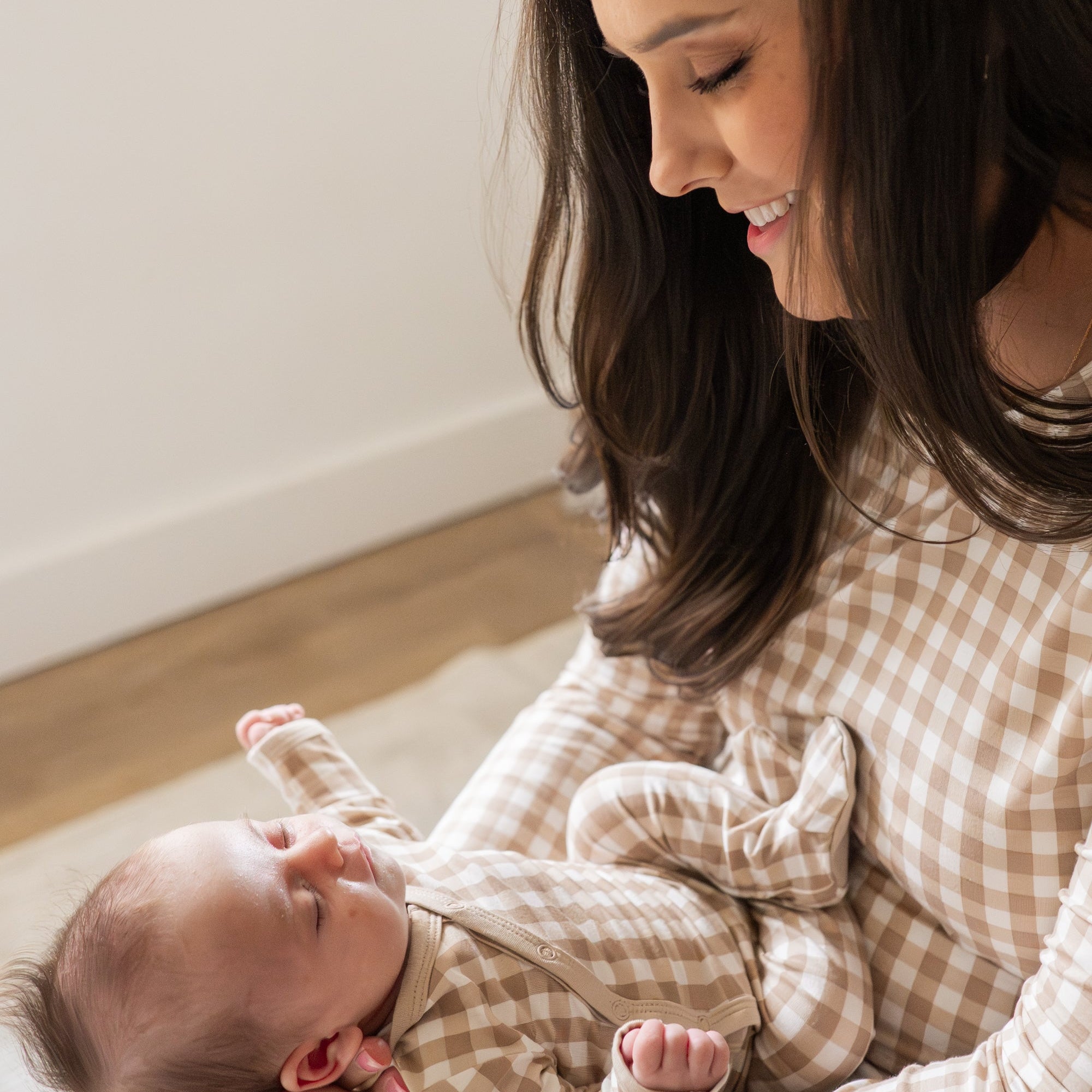 Mother wearing the Women's Jogger Pajama Set in Bisque Gingham holding her matching newborn in her hands smiling down at her